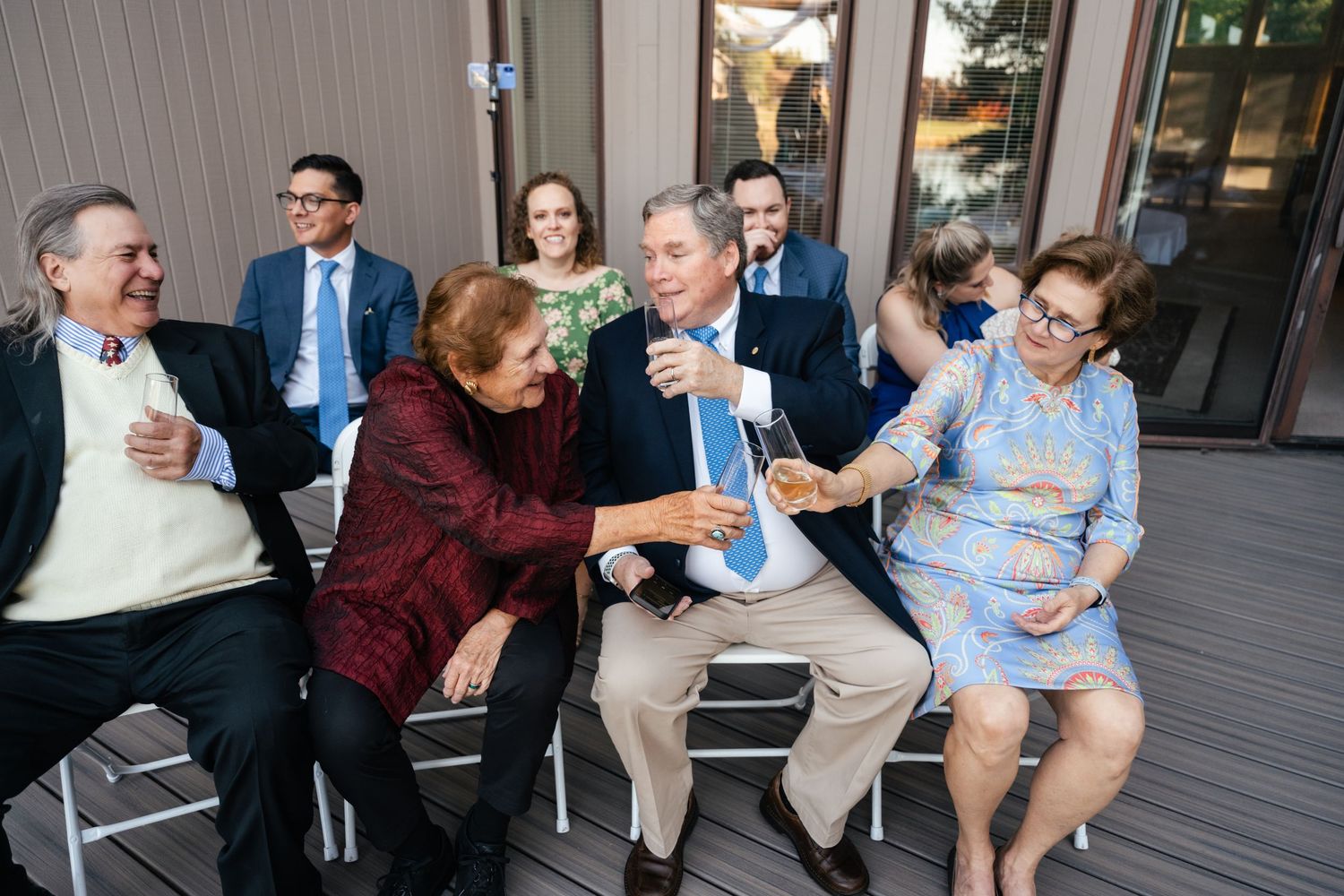 A group of people sitting on chairs outdoors share laughter and conversation during a casual gathering.