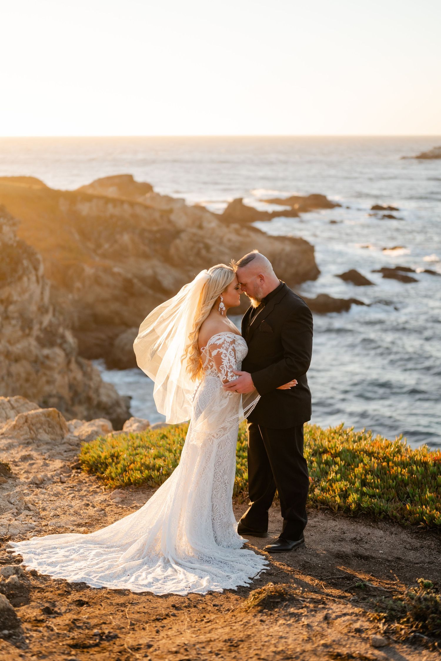 Newlyweds share tender moments during a golden hour photoshoot on a dramatic oceanside cliff.