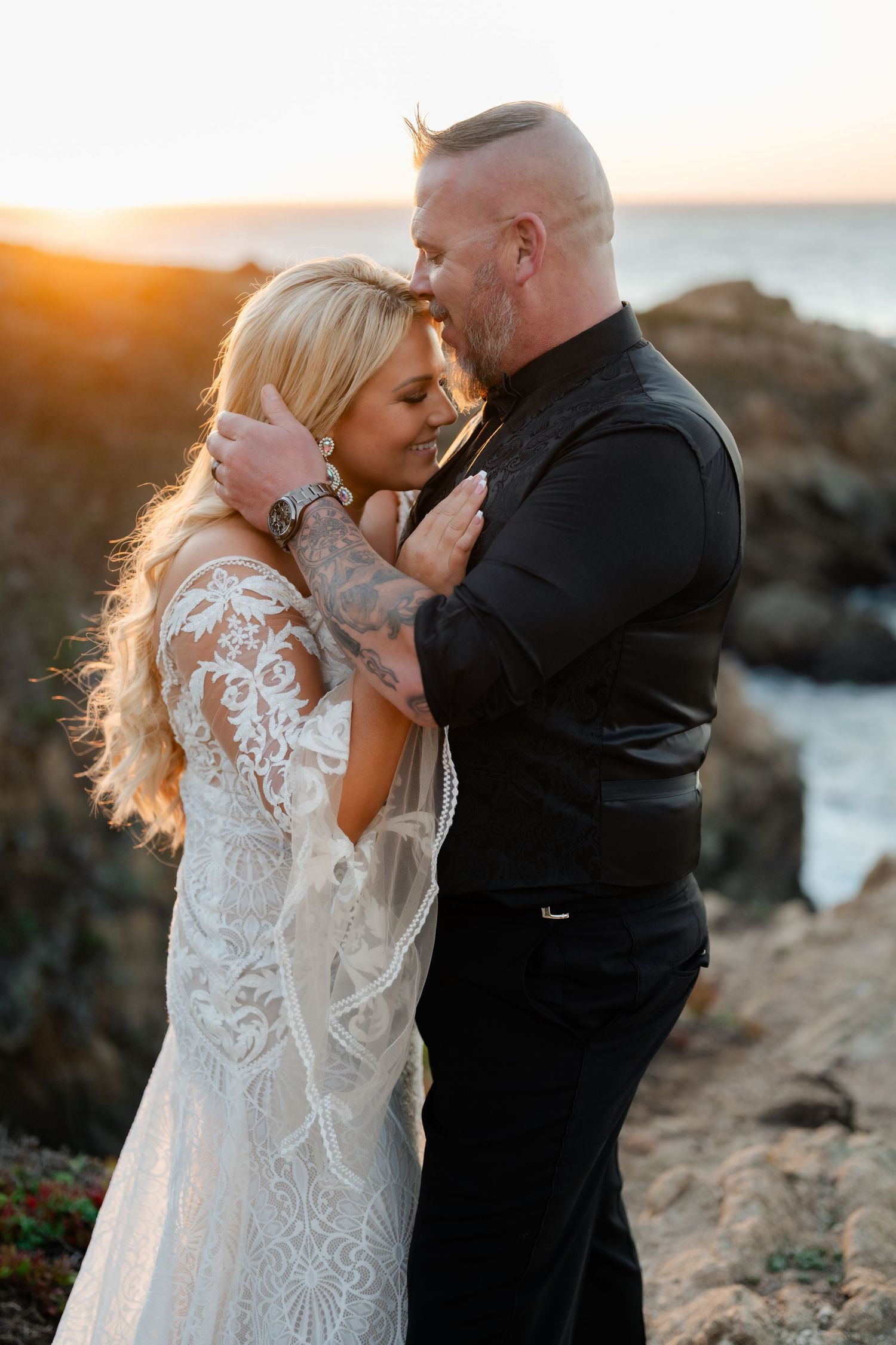 A romantic sunset moment between newlyweds on a rocky coastal cliff.