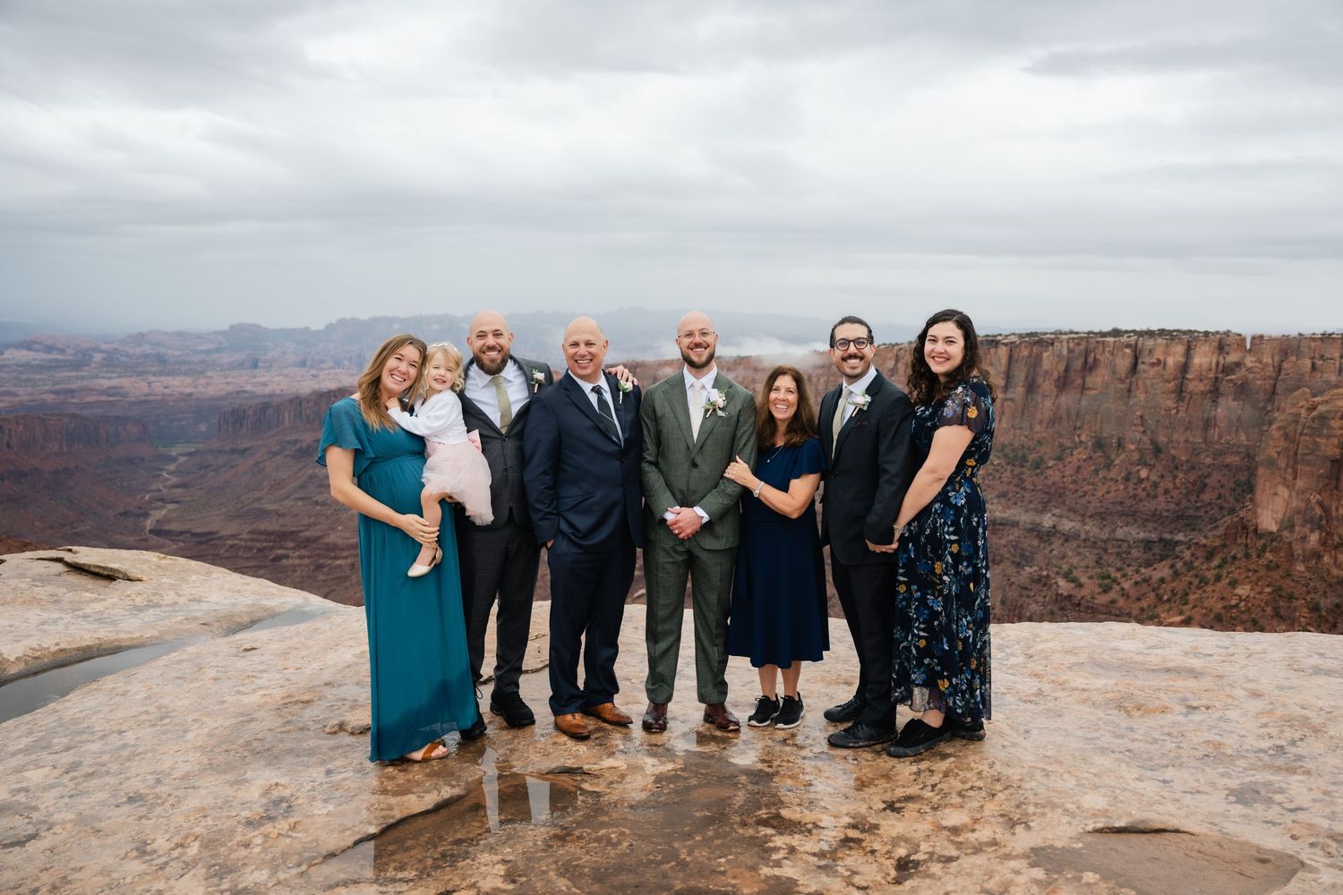 Wedding party poses on scenic overlook at Grand Canyon with dramatic red rock cliffs in background.