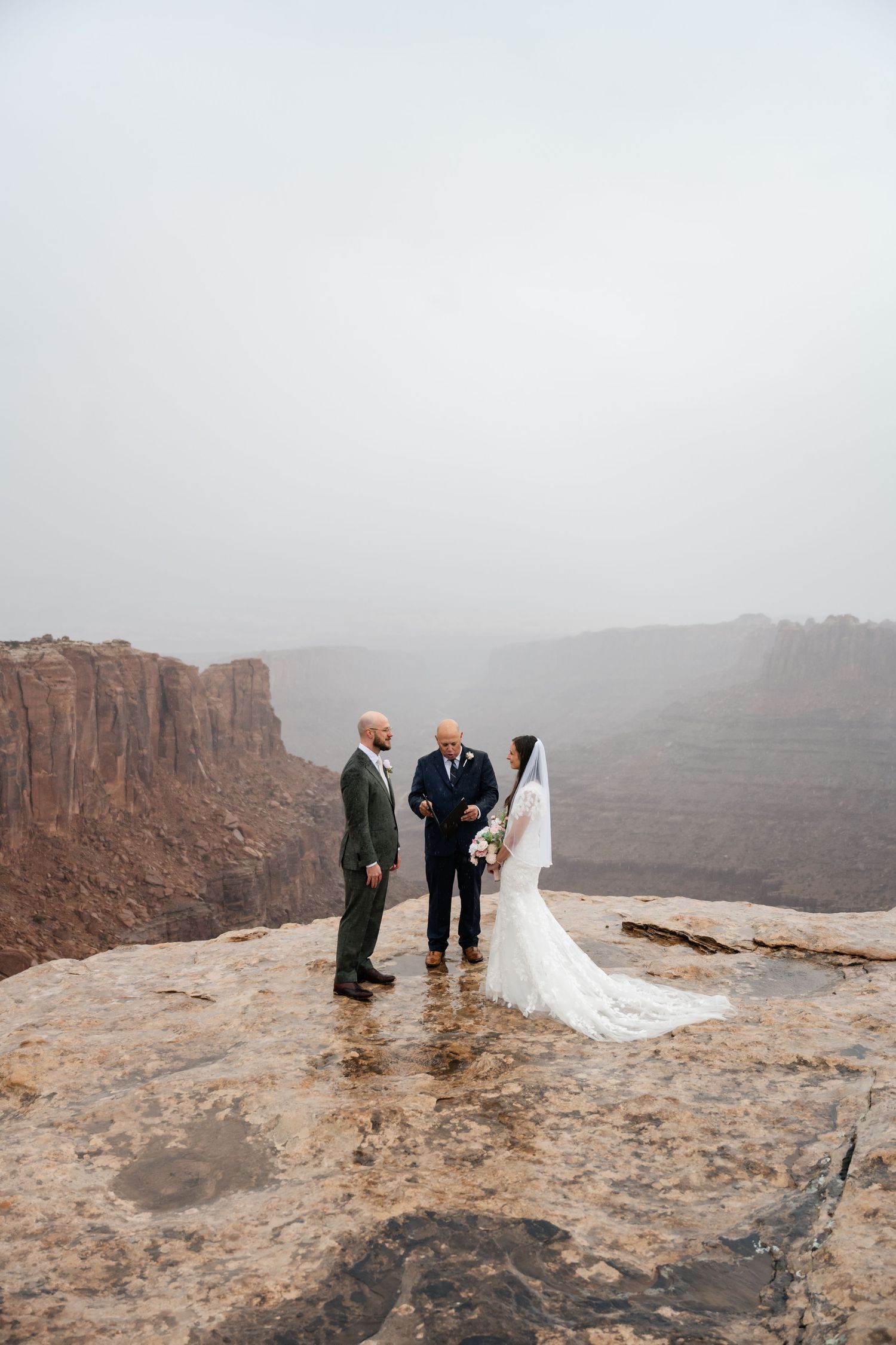 Wedding ceremony participants standing on wet rocky overlook with dramatic canyon views.