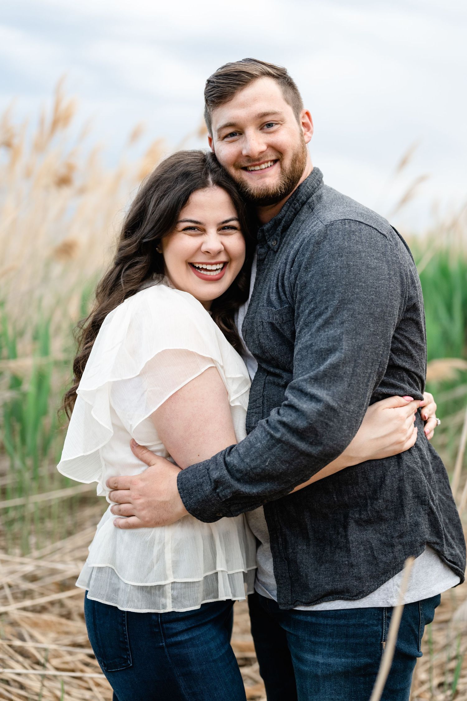 A happy couple embraces while laughing in a field of tall grasses.