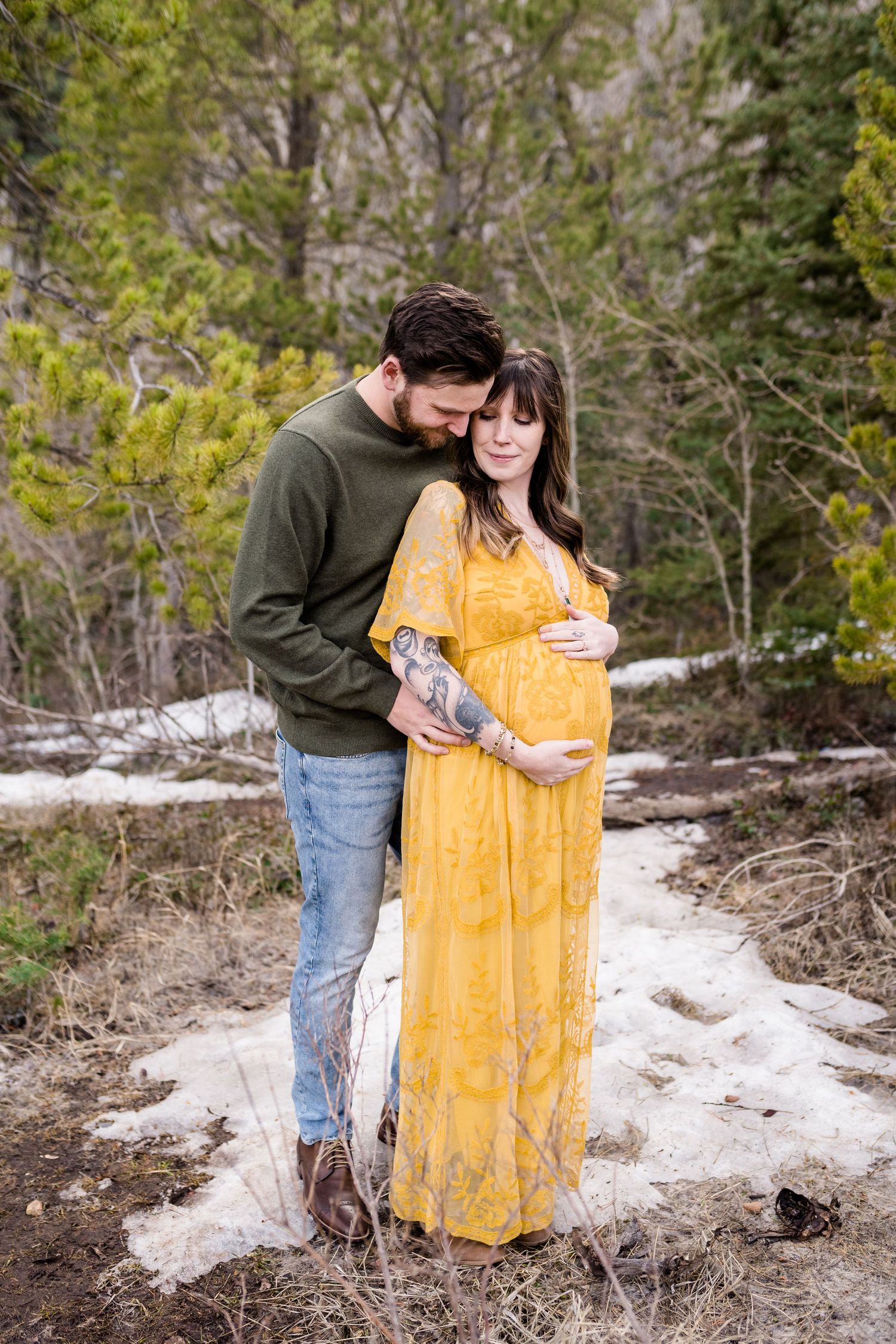 A couple in a snowy forest setting share intimate moments, with one person wearing a flowing yellow dress and the other in green.