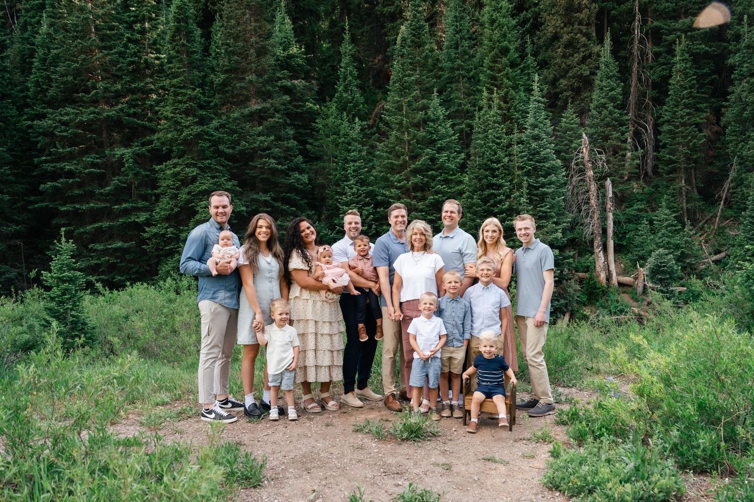A large group poses for photos in a lush forest setting wearing coordinated casual outfits in neutral tones.