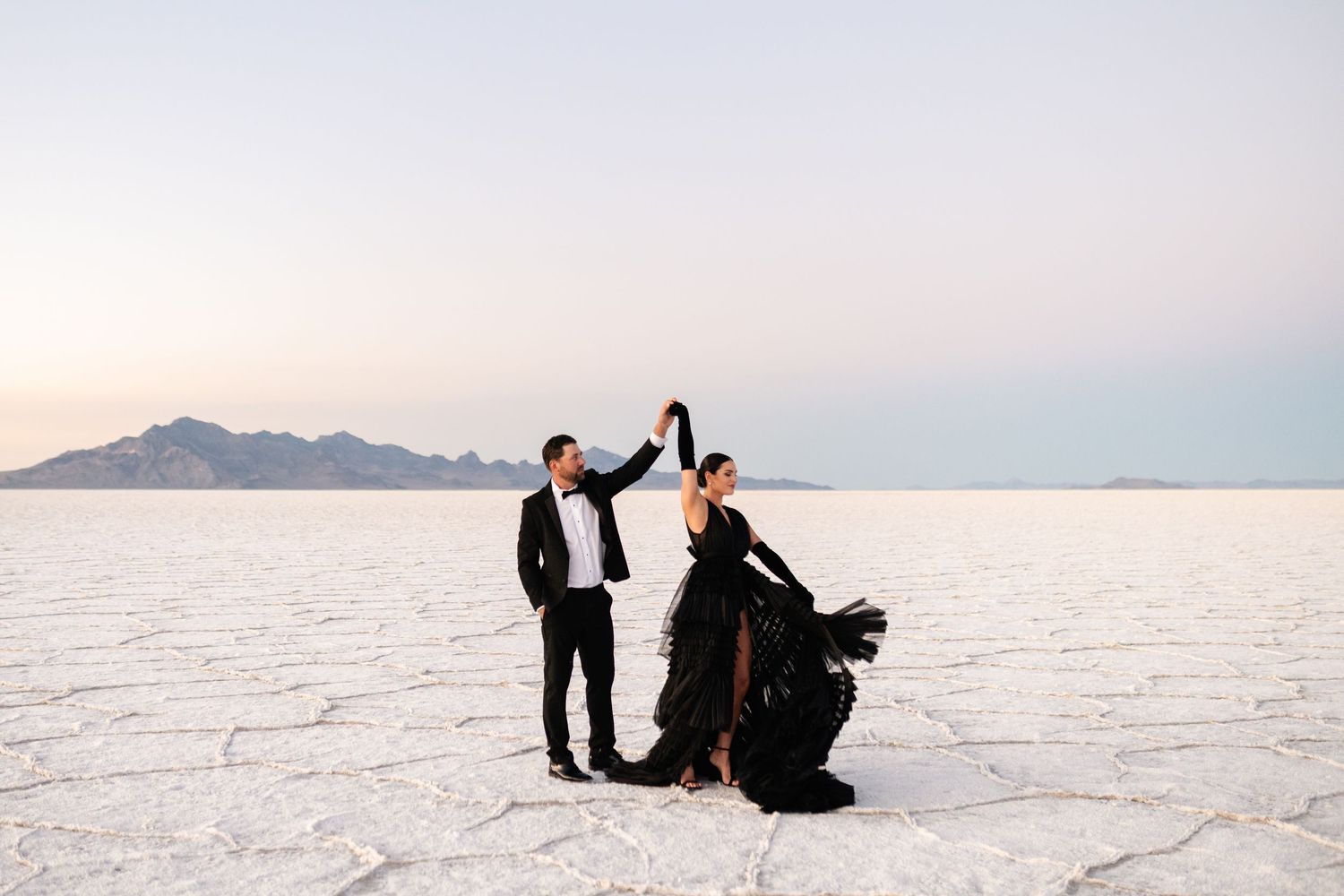 Utah Salt Flats Photographer. Elegant couple creates romantic moments while posing on vast white salt flats at dusk.