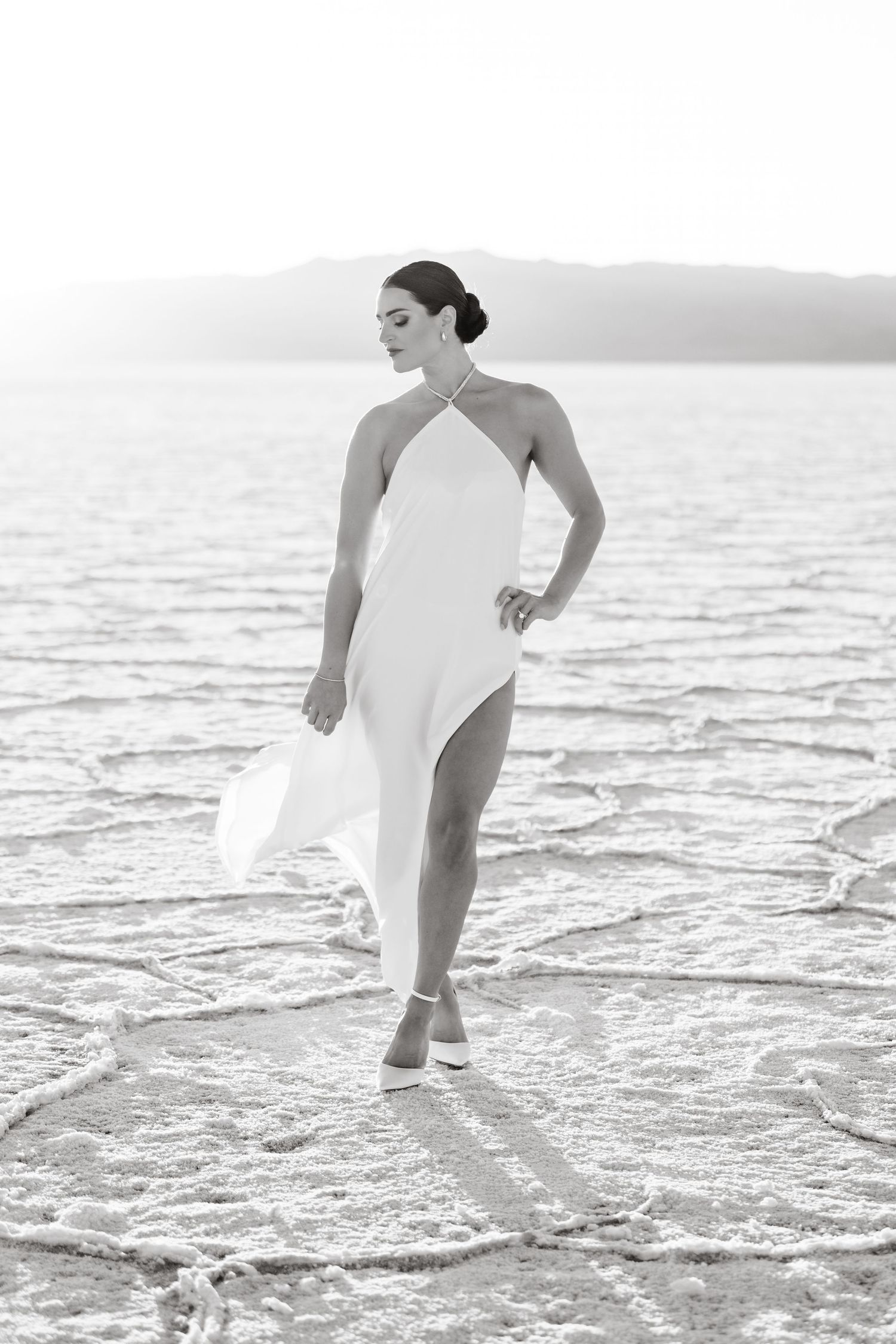 Salt Flats Photographer. Woman in white dress walking gracefully across salt flats during a photo session at sunset.