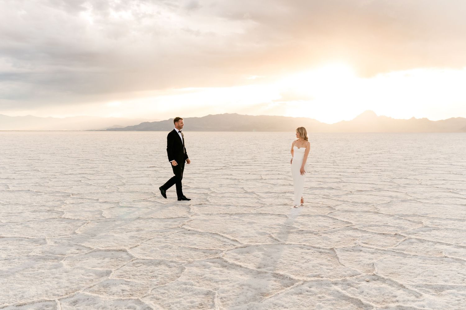 A person walks across a vast snow-covered landscape beneath a cloudy sunset sky.Salt Flats Elopement Photographer.