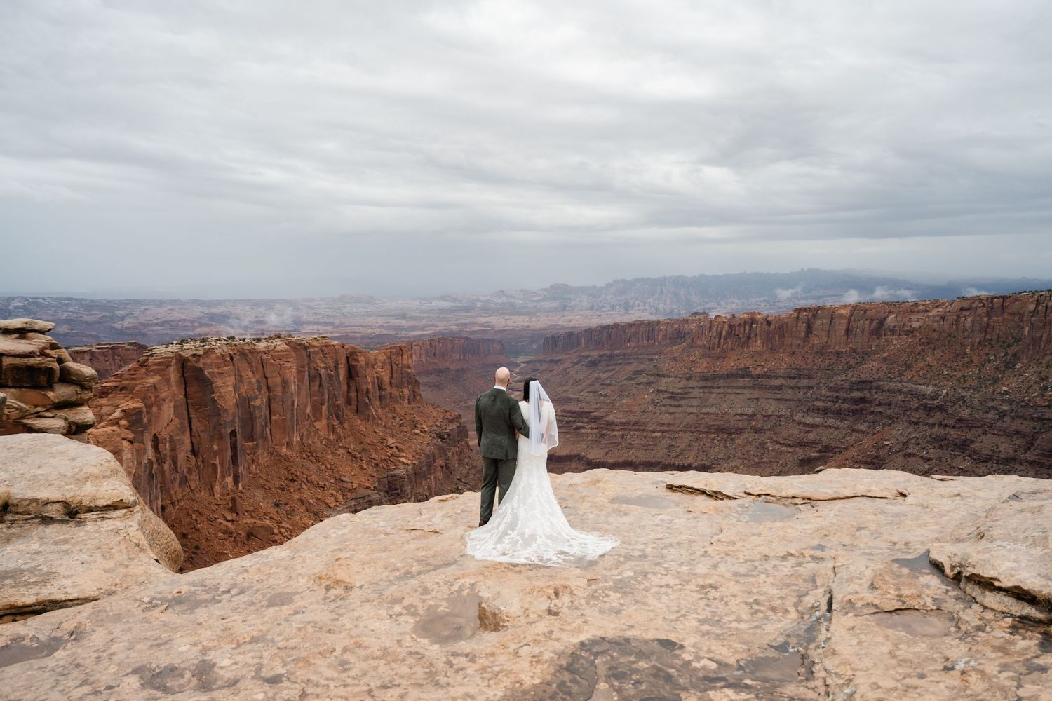 Wide angle landscape shot of a wedding photo session on the edge of a dramatic desert canyon.