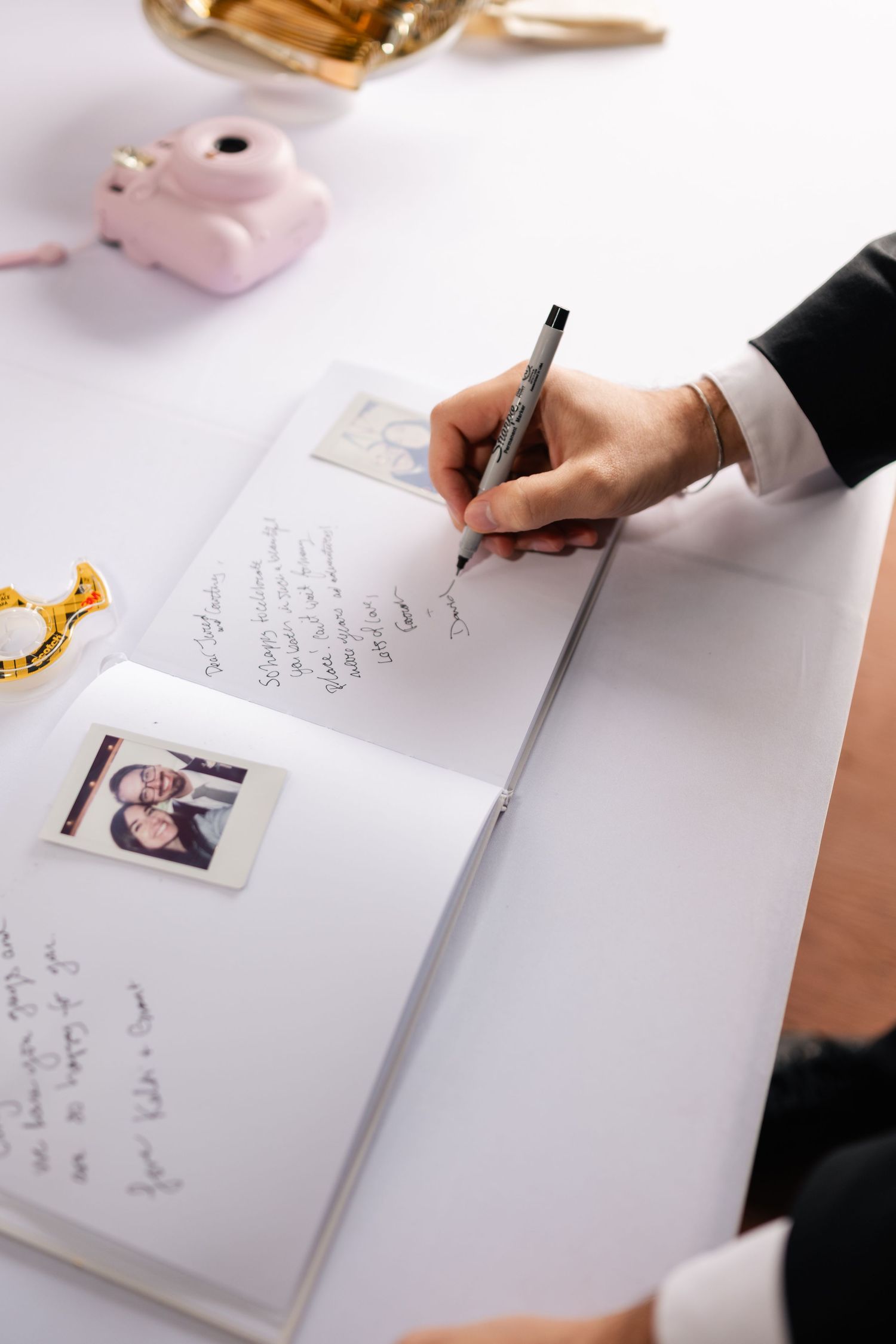Hands writing personal messages in a wedding guest book with a fountain pen and photographs.