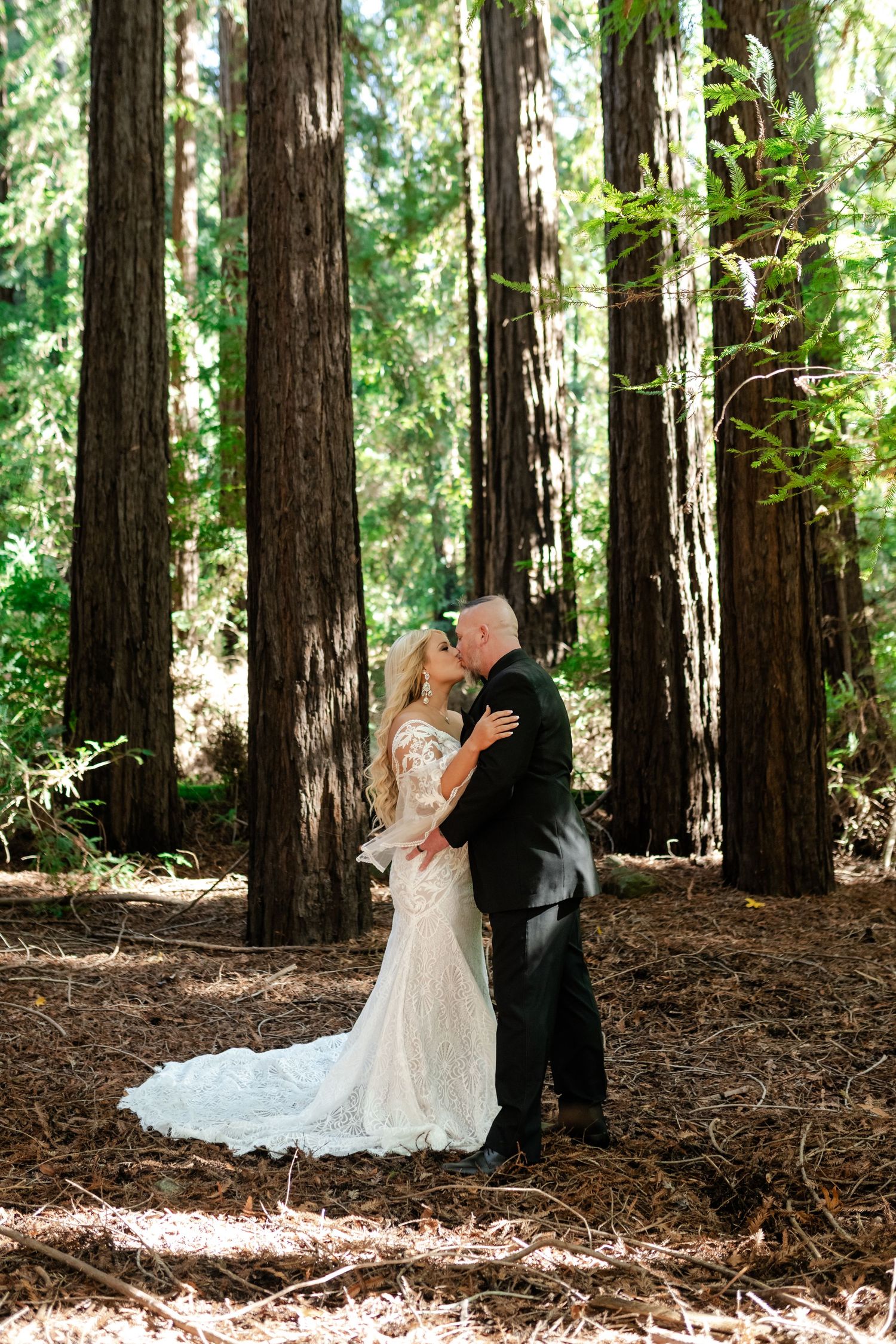 A romantic wedding moment captured among tall redwood trees in a forest.