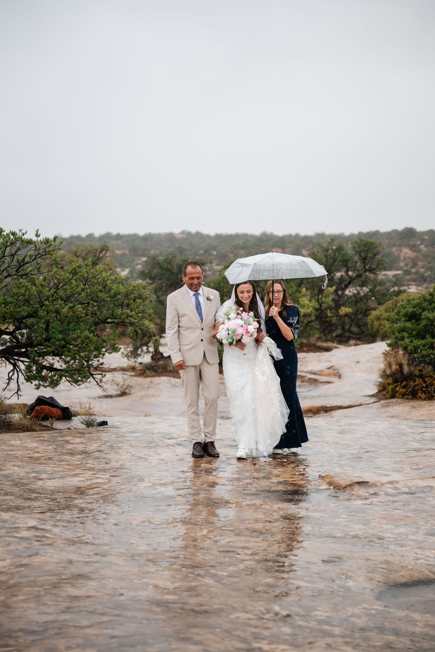 Wedding party stands in flood waters during rainy outdoor ceremony with white umbrella and formal attire.