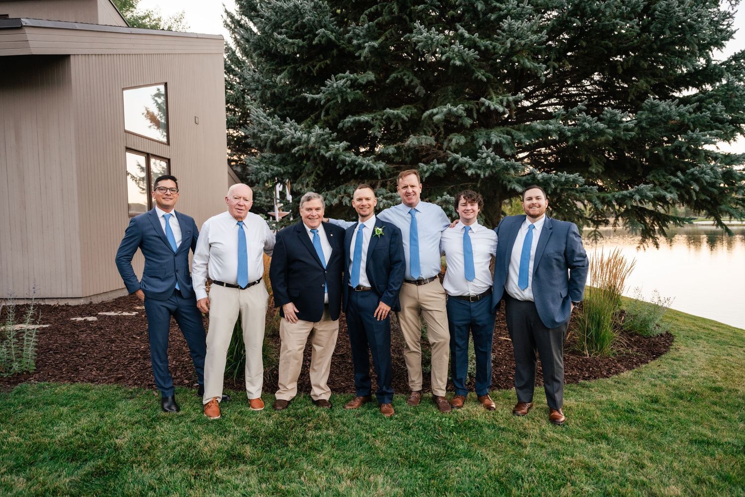 Group of formally dressed men standing together outdoors for wedding party photo.
