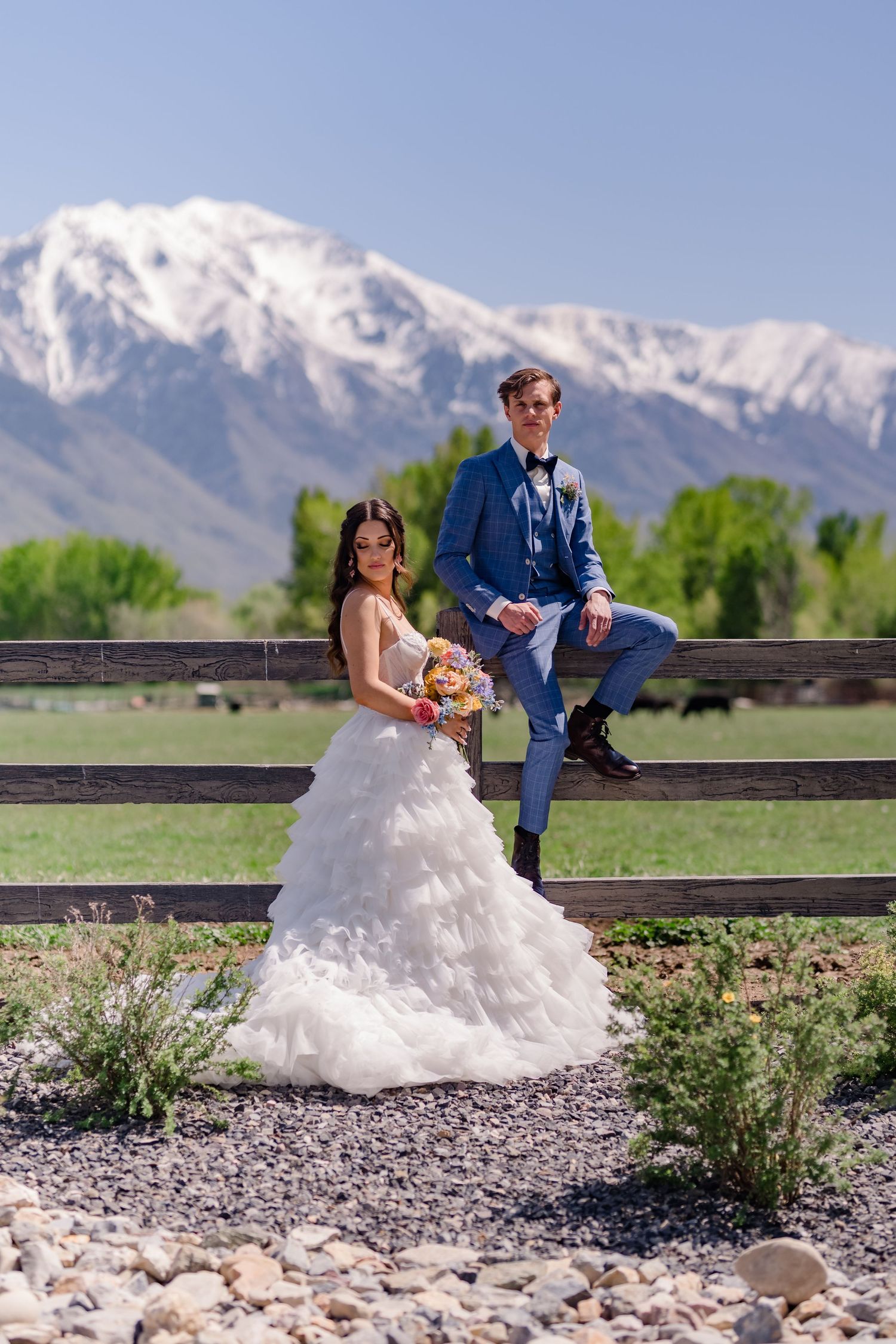 Snow-capped mountains provide a majestic backdrop to a scenic rural landscape with wooden fencing.