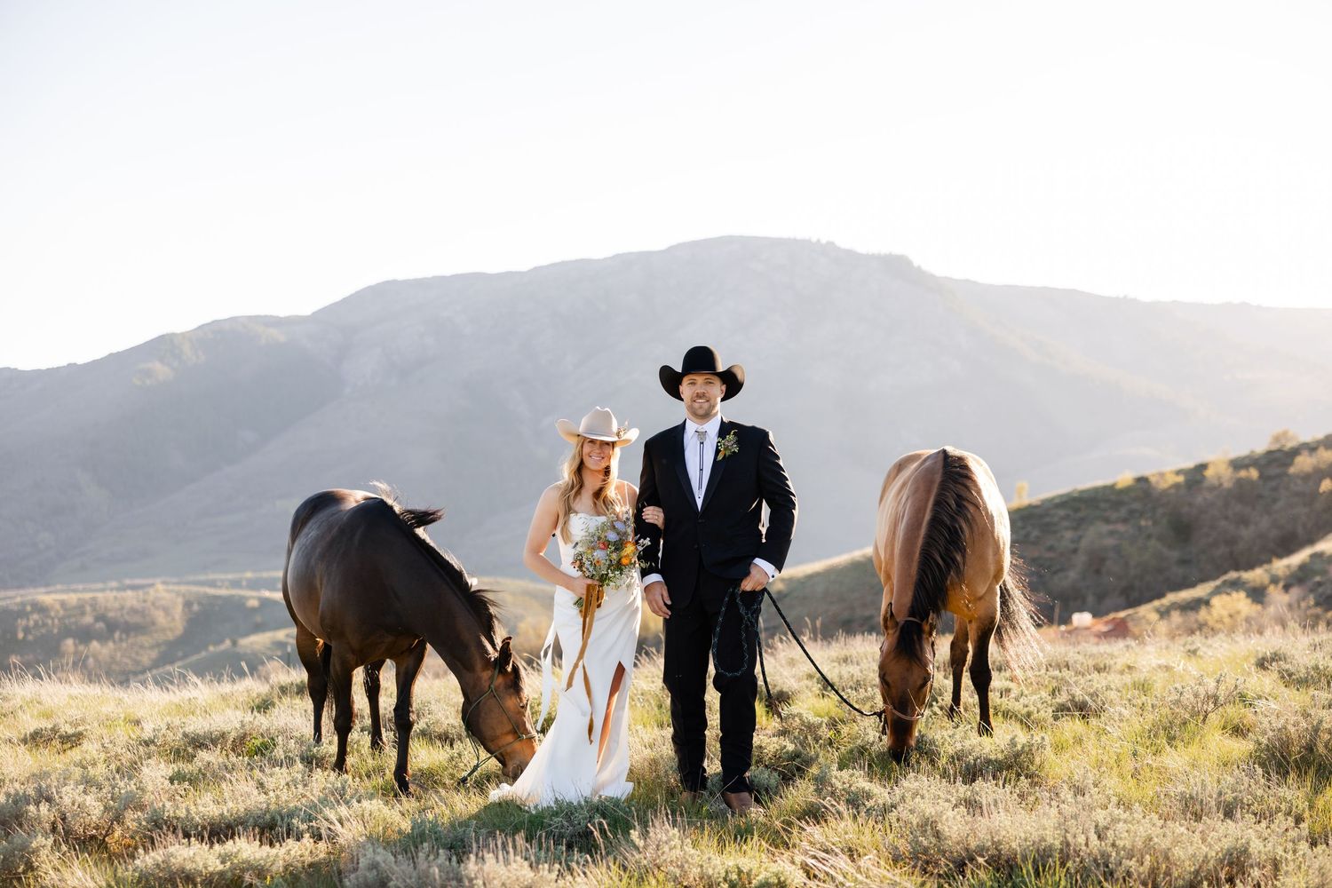 A couple shares an intimate moment with their horses in a scenic mountain meadow during golden hour. Utah mountain elopement photographer.