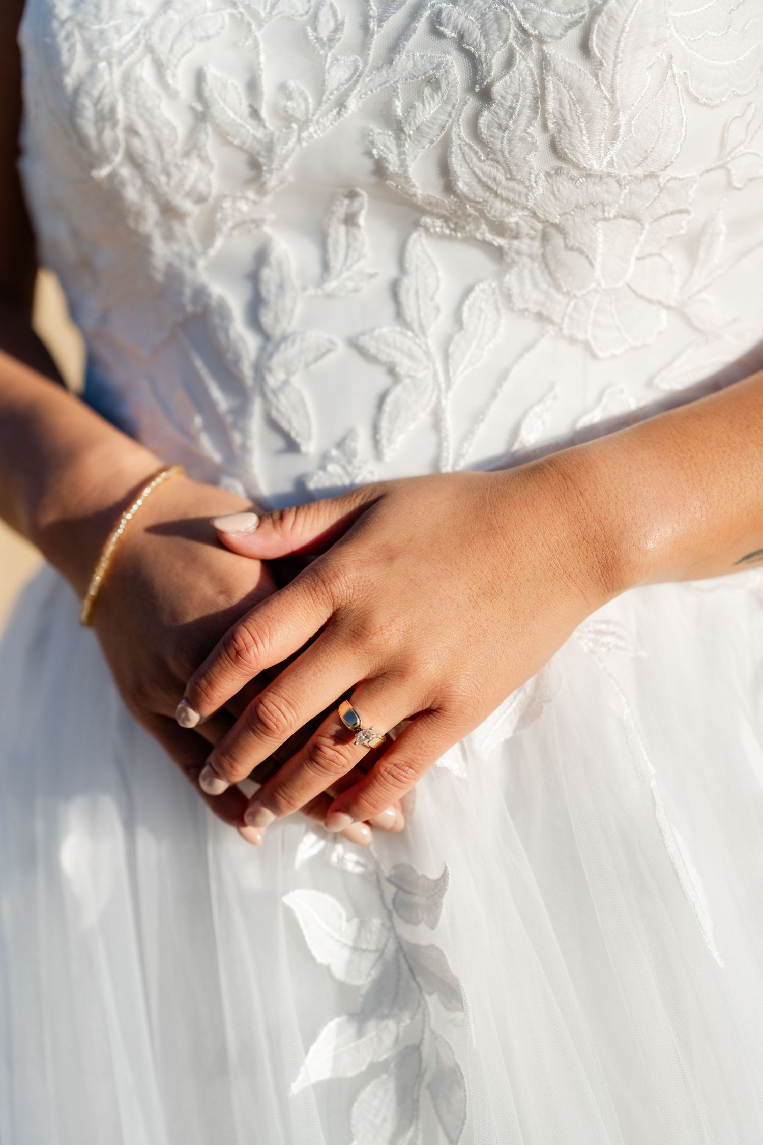 Close-up details of hands touching delicate white lace wedding dress fabric.