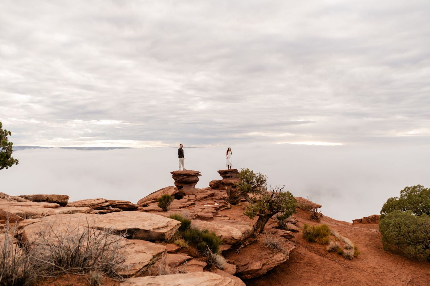 Wide angle view of red rock formations under cloudy skies in a desert landscape.