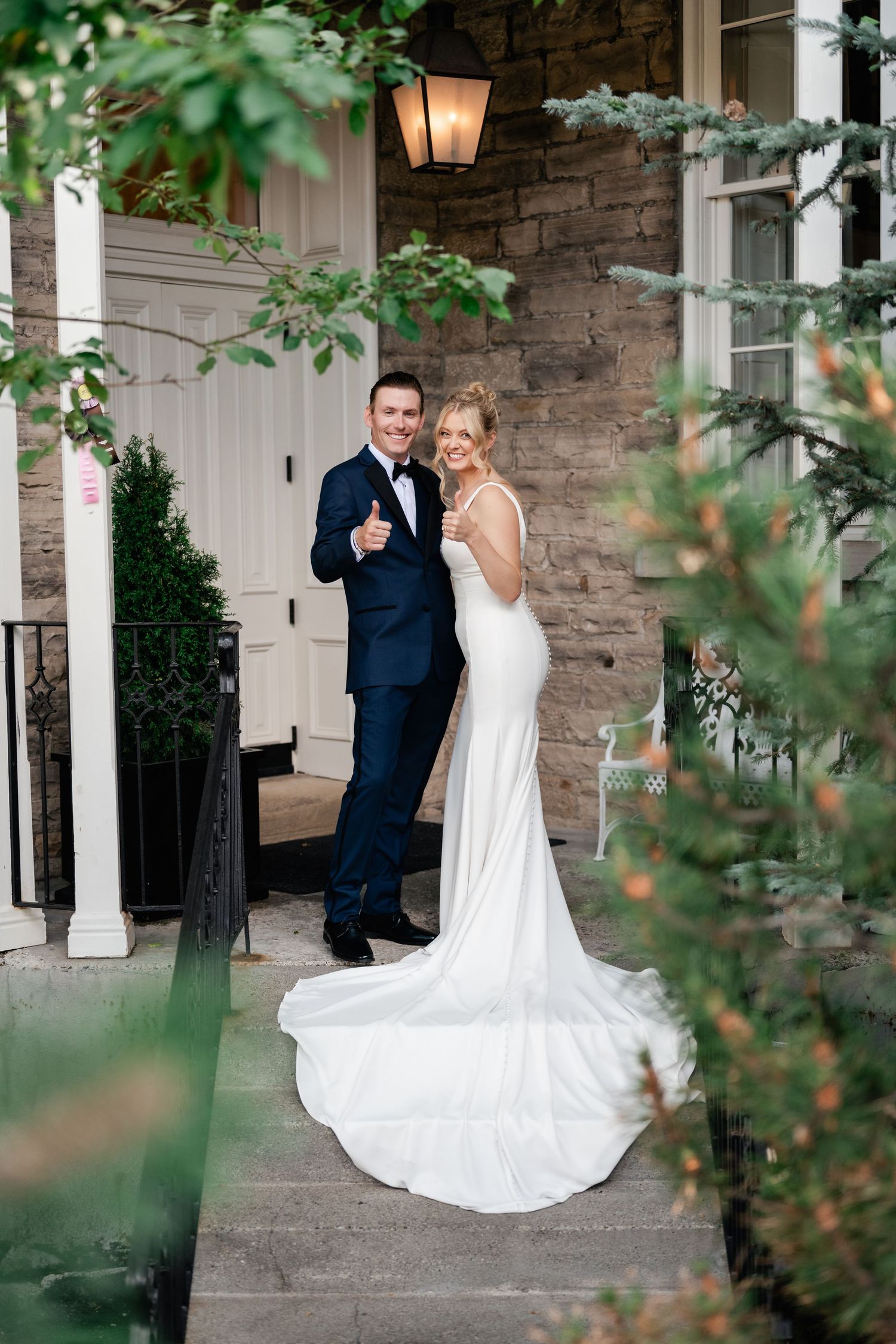 A couple shares a joyful moment together on their wedding day outside a stone building with greenery.