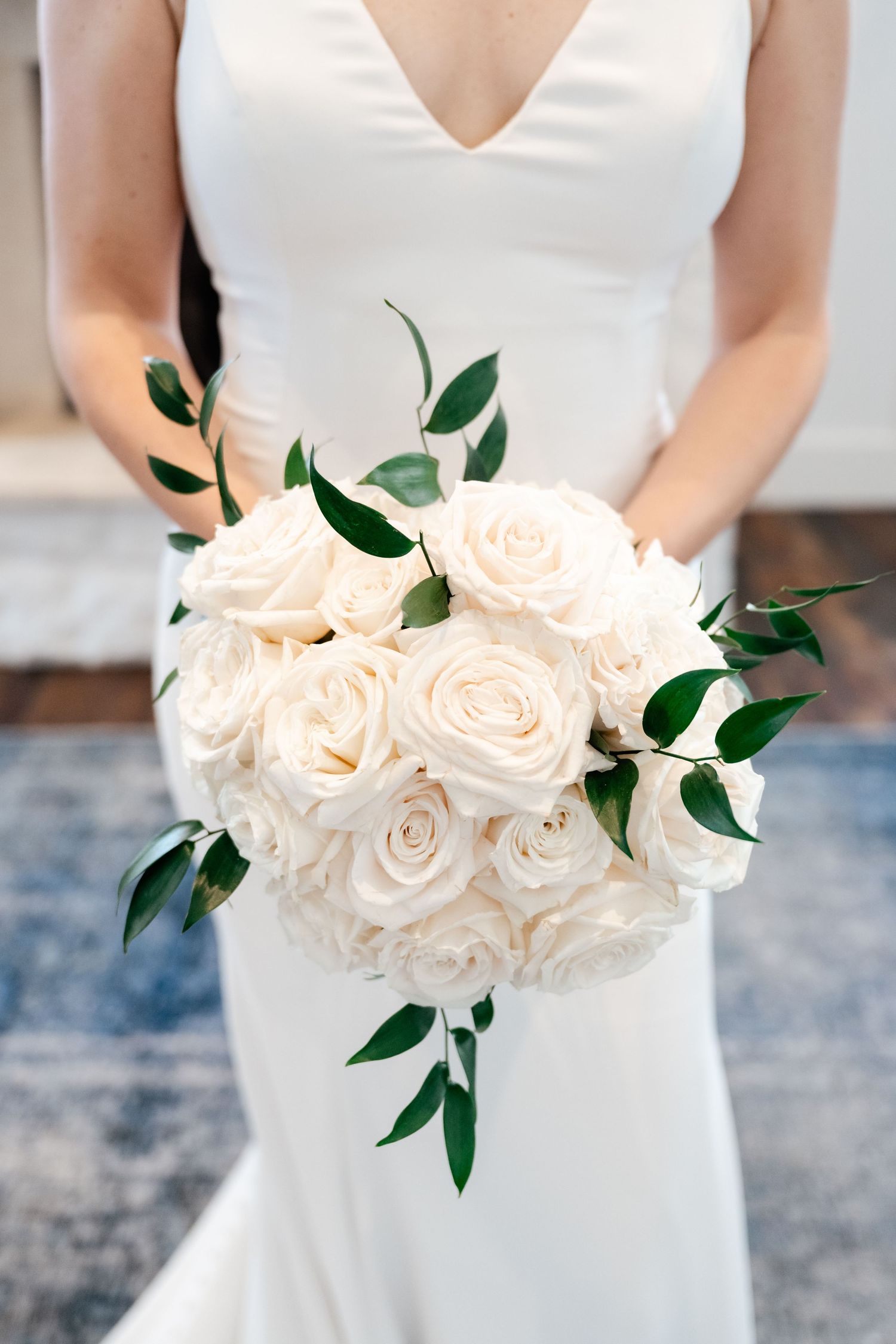 Elegant white bridal bouquet featuring cream roses and green foliage held against a white dress.