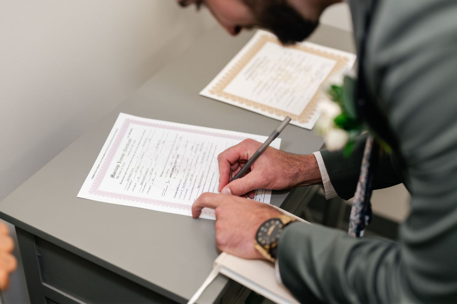 Close-up view of hands writing on official documents at a modern office desk.