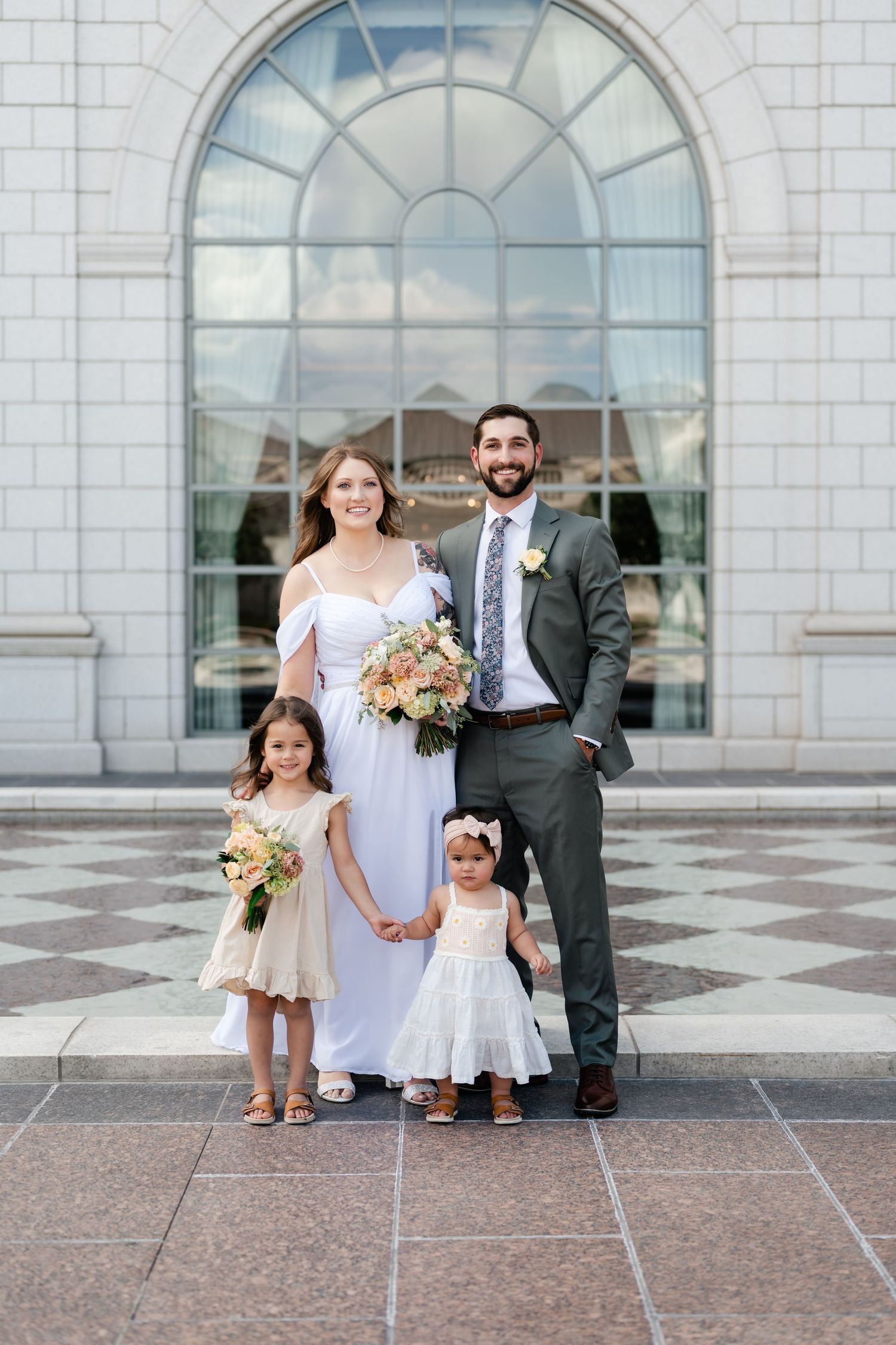 Family gathers for wedding photos outside grand white stone building with arched windows and marble flooring.