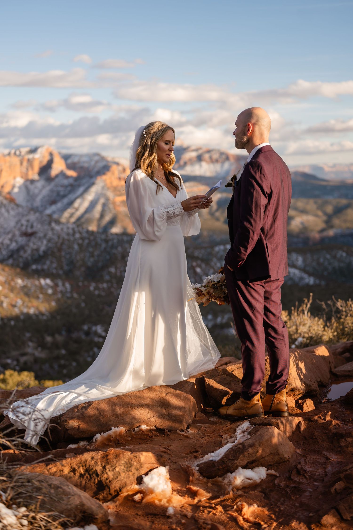 Intimate wedding ceremony on red rock overlook with snow-capped mountains in distance.