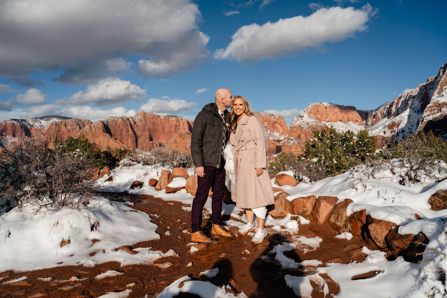 Panoramic winter vista of snow-covered red rock formations under a bright blue sky.