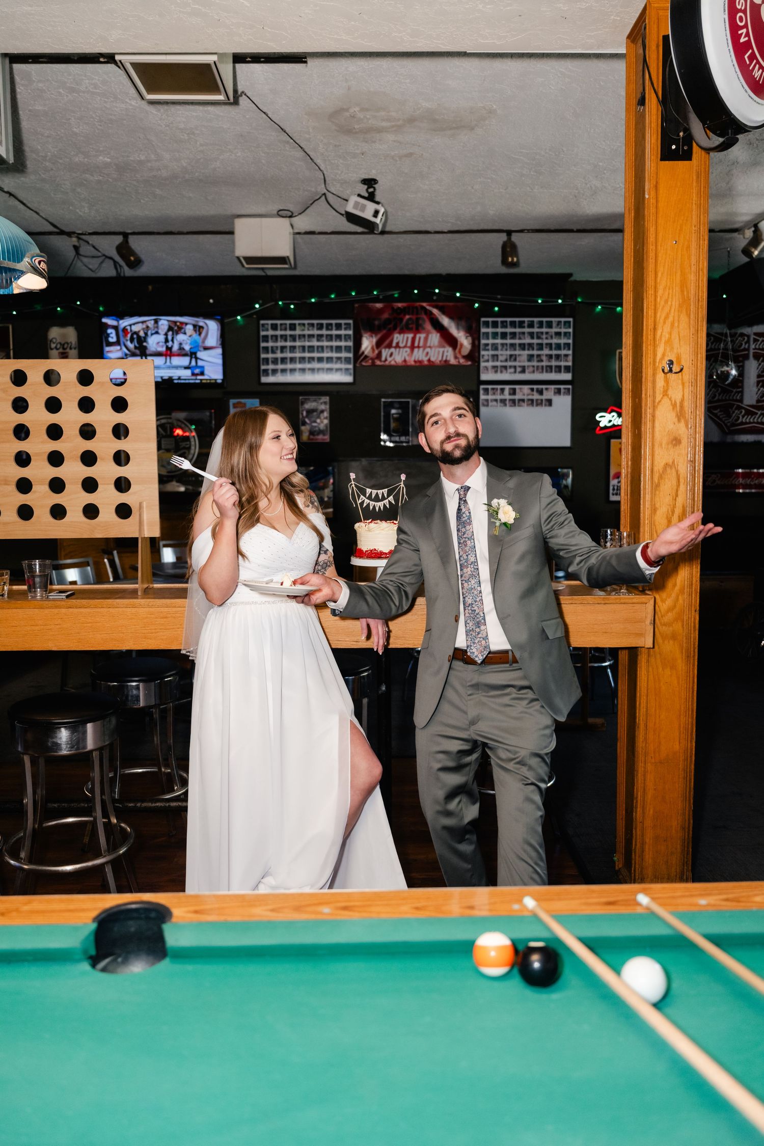 A couple playfully poses and dances together while playing pool at a casual bar venue.