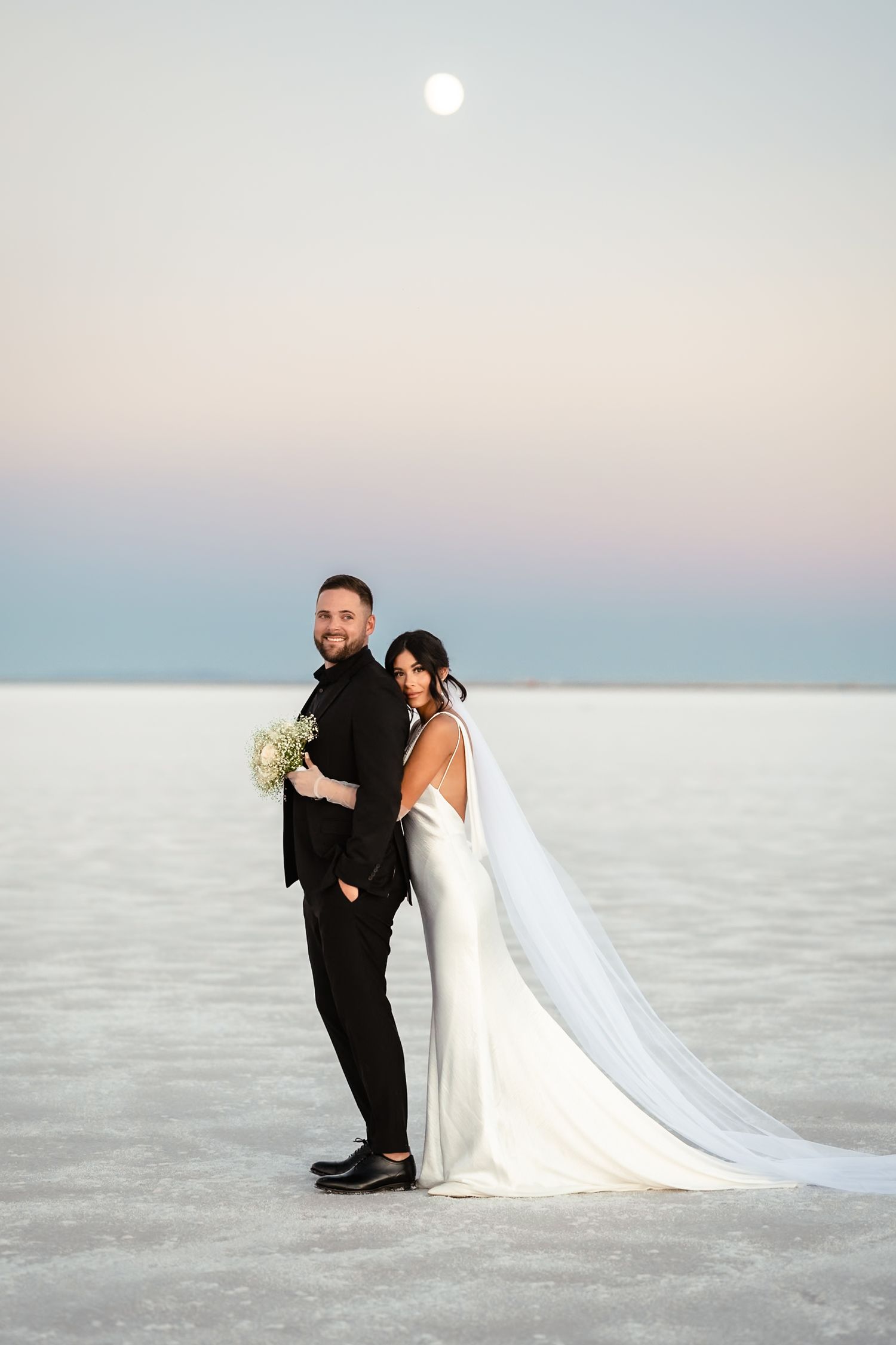 A couple shares a romantic moment on the stark white salt flats during sunset.