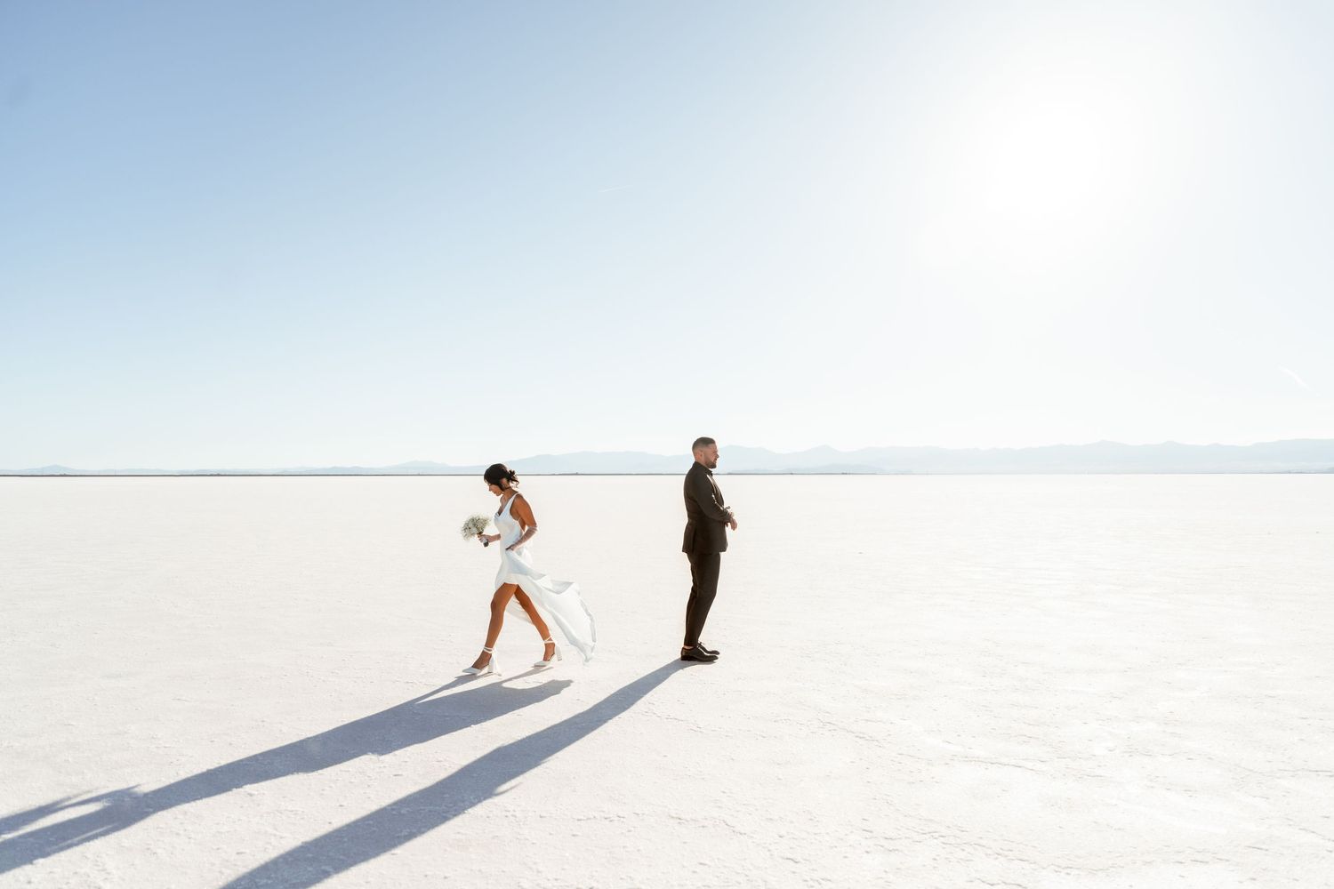 People cast long shadows while walking across pristine white sand at Bonneville Salt Flats during sunset.