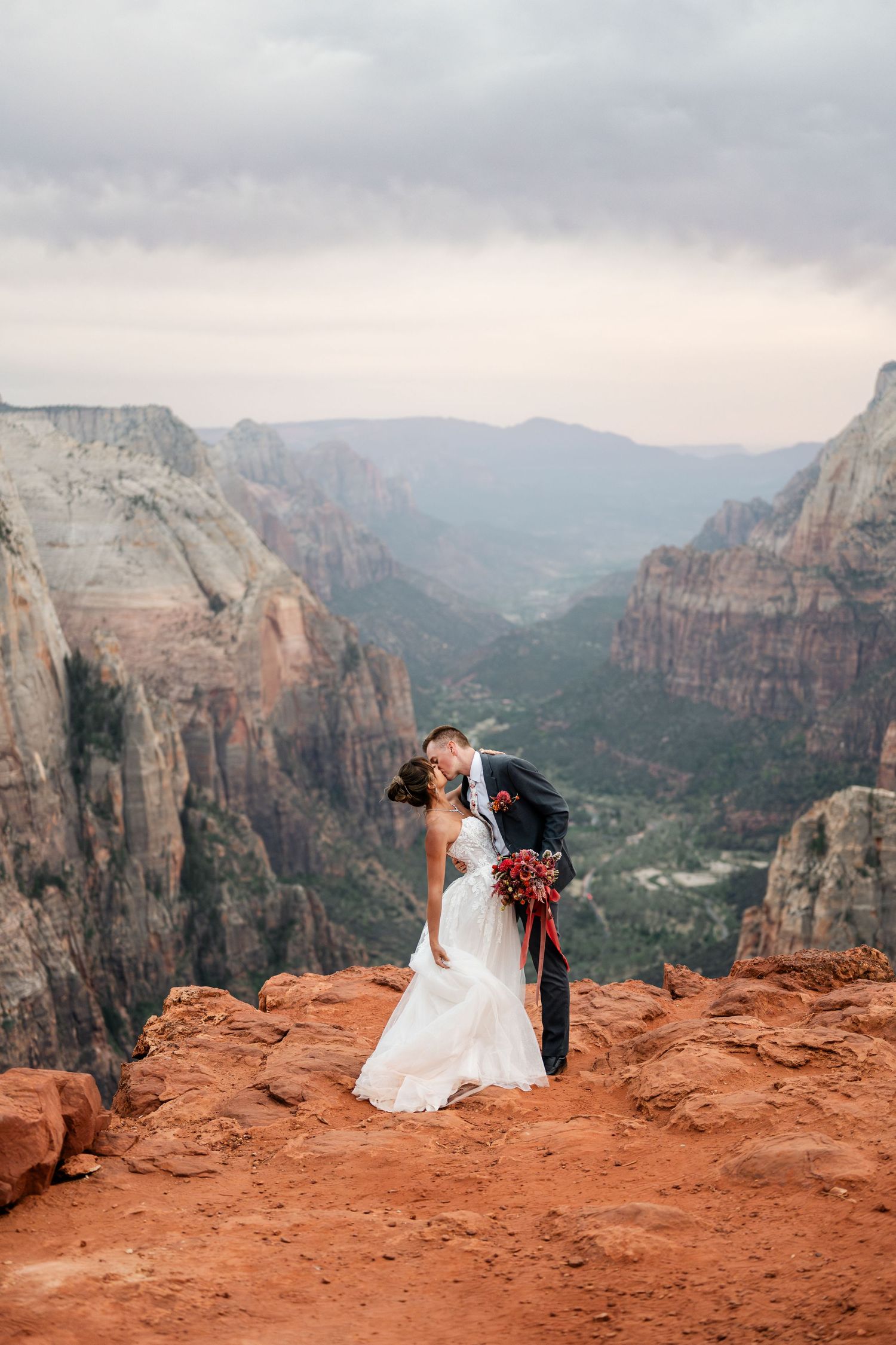A wedding couple shares an intimate moment on the red rocks overlooking Zion National Park's dramatic canyon landscape.