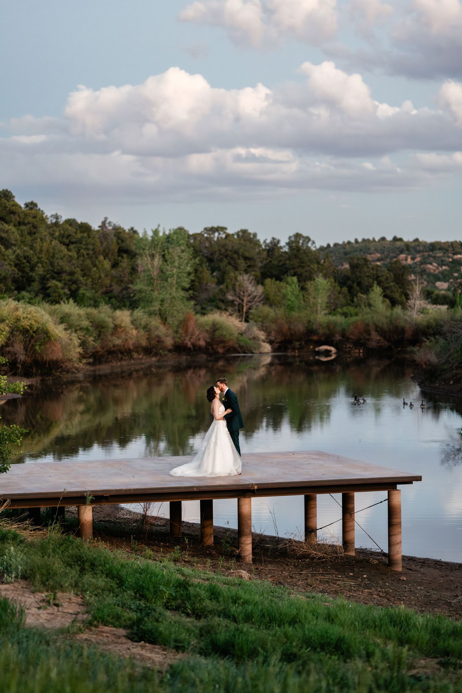 Scenic lakeside wooden pier with calm water reflections and lush greenery. Drone photography by Utah Wedding Photographer.