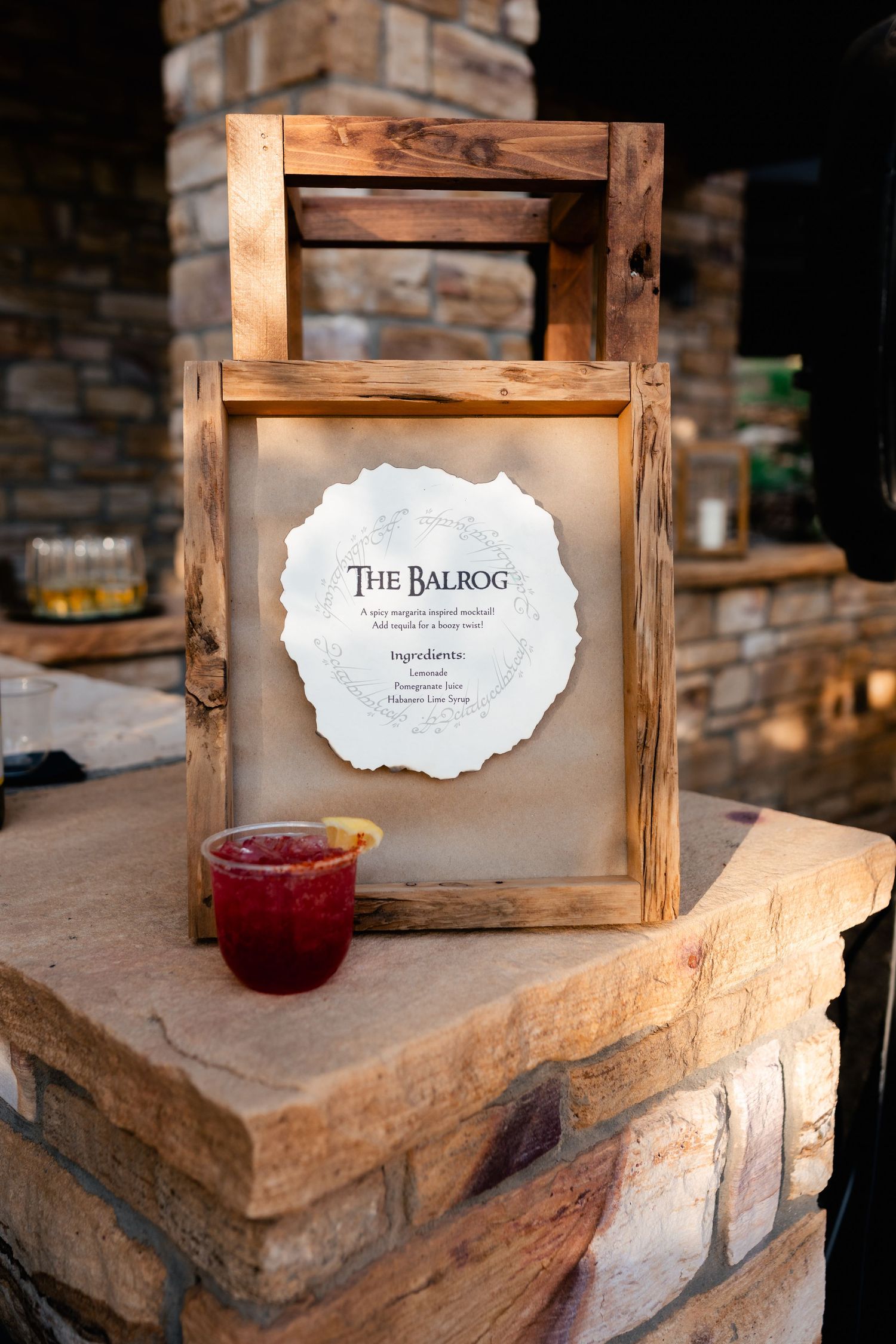 Rustic wooden frames with wedding signage displayed on stone ledges with a red beverage.