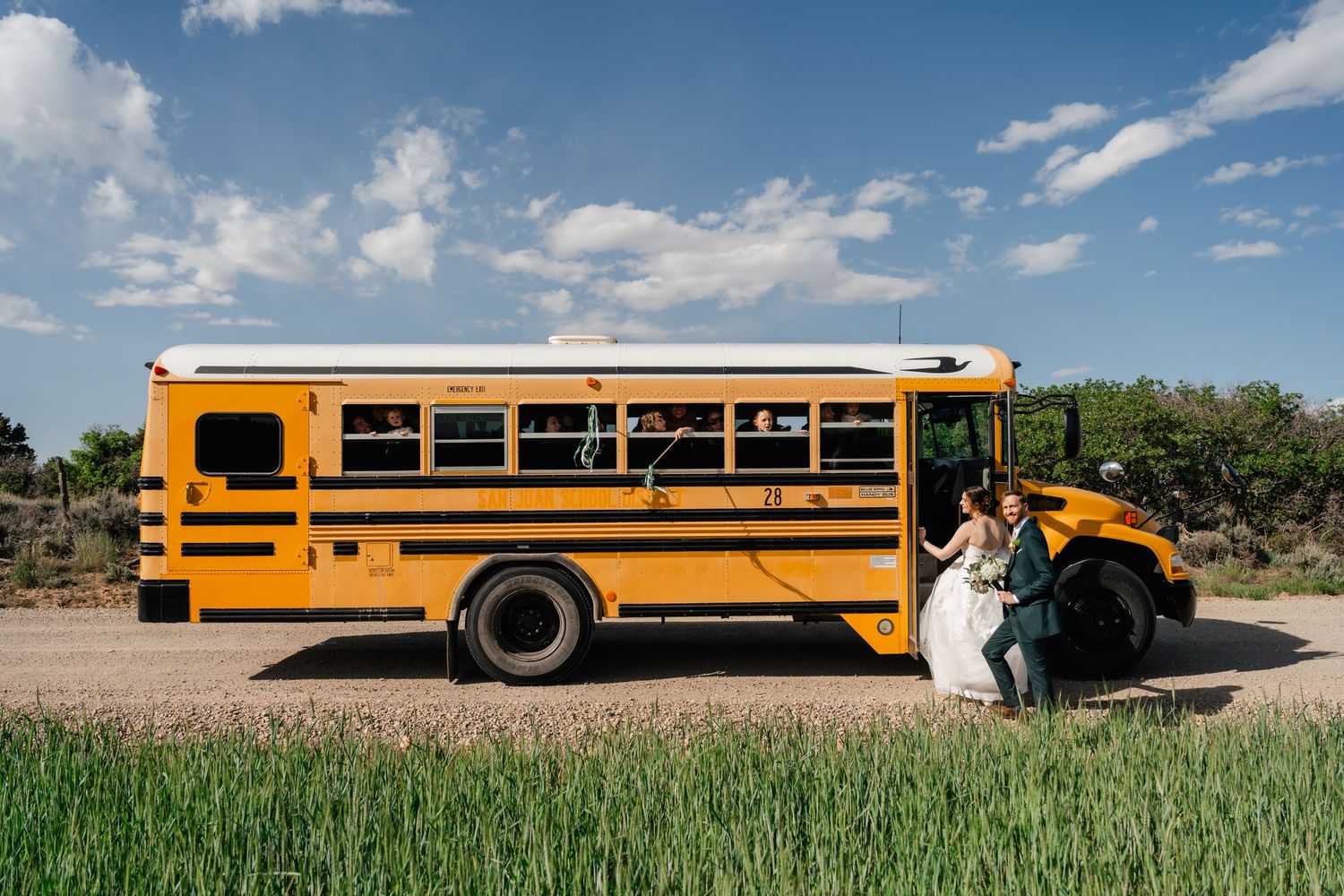 Six identical yellow school buses parked in a row against blue sky and rural landscape backgrounds.