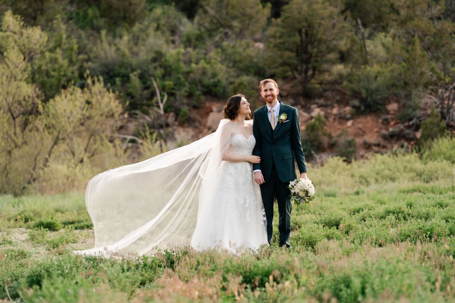 Wedding couple walking through green spring meadow with flowing white dress.