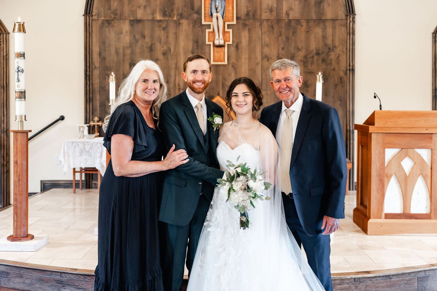 Wedding party poses in front of a rustic wooden church altar with cross and stained glass windows.