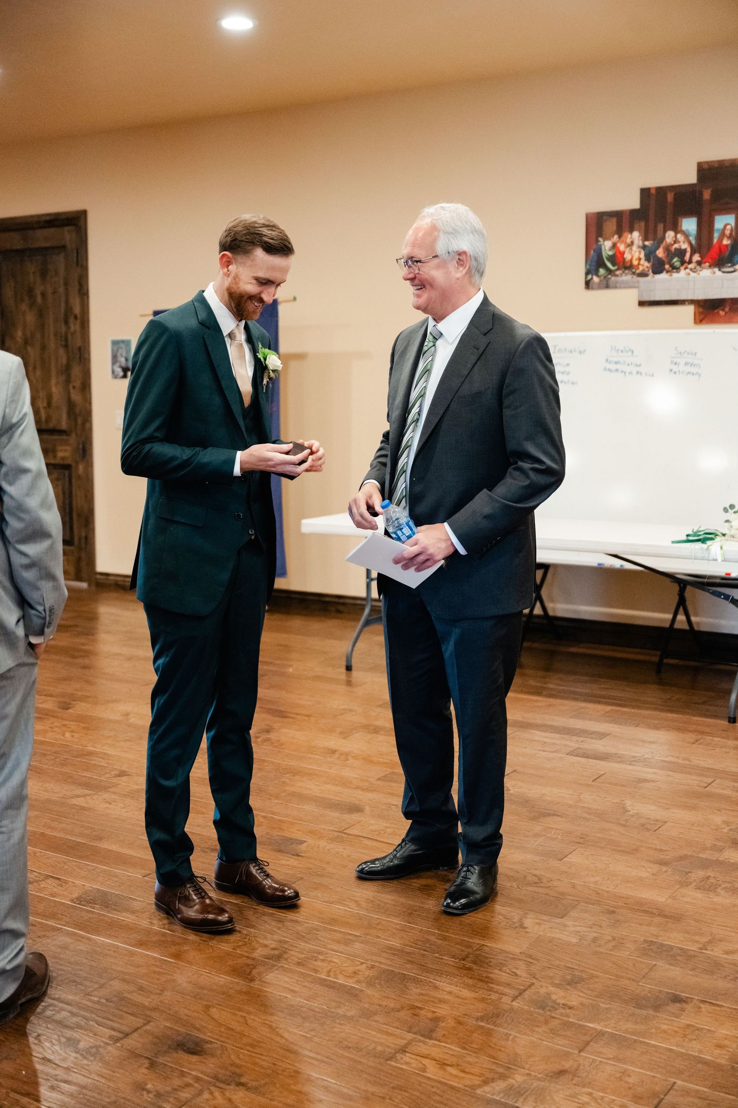 Men in formal attire gather on hardwood floor before wedding ceremony.