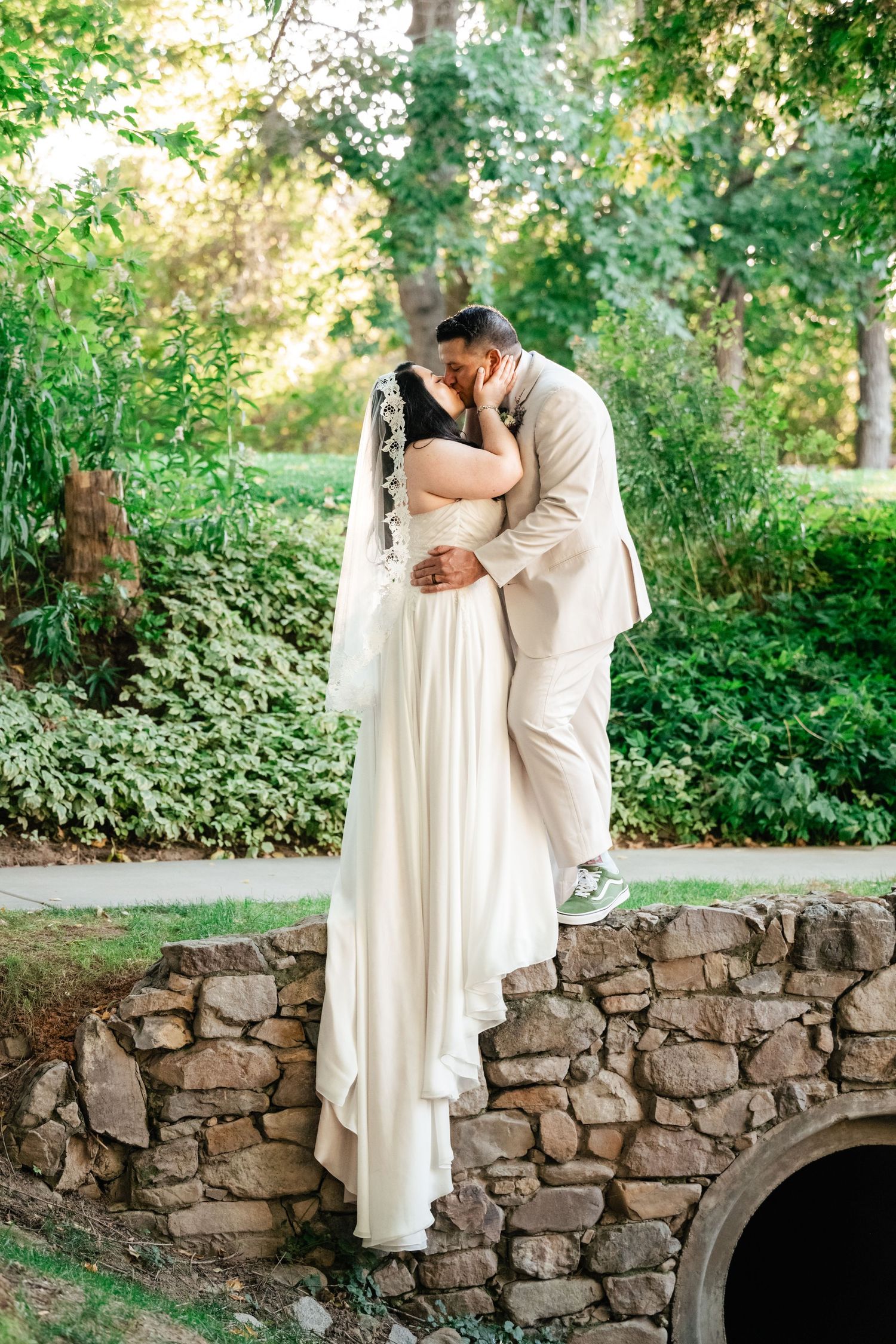 A romantic wedding moment captured on a stone bridge with greenery in the background.