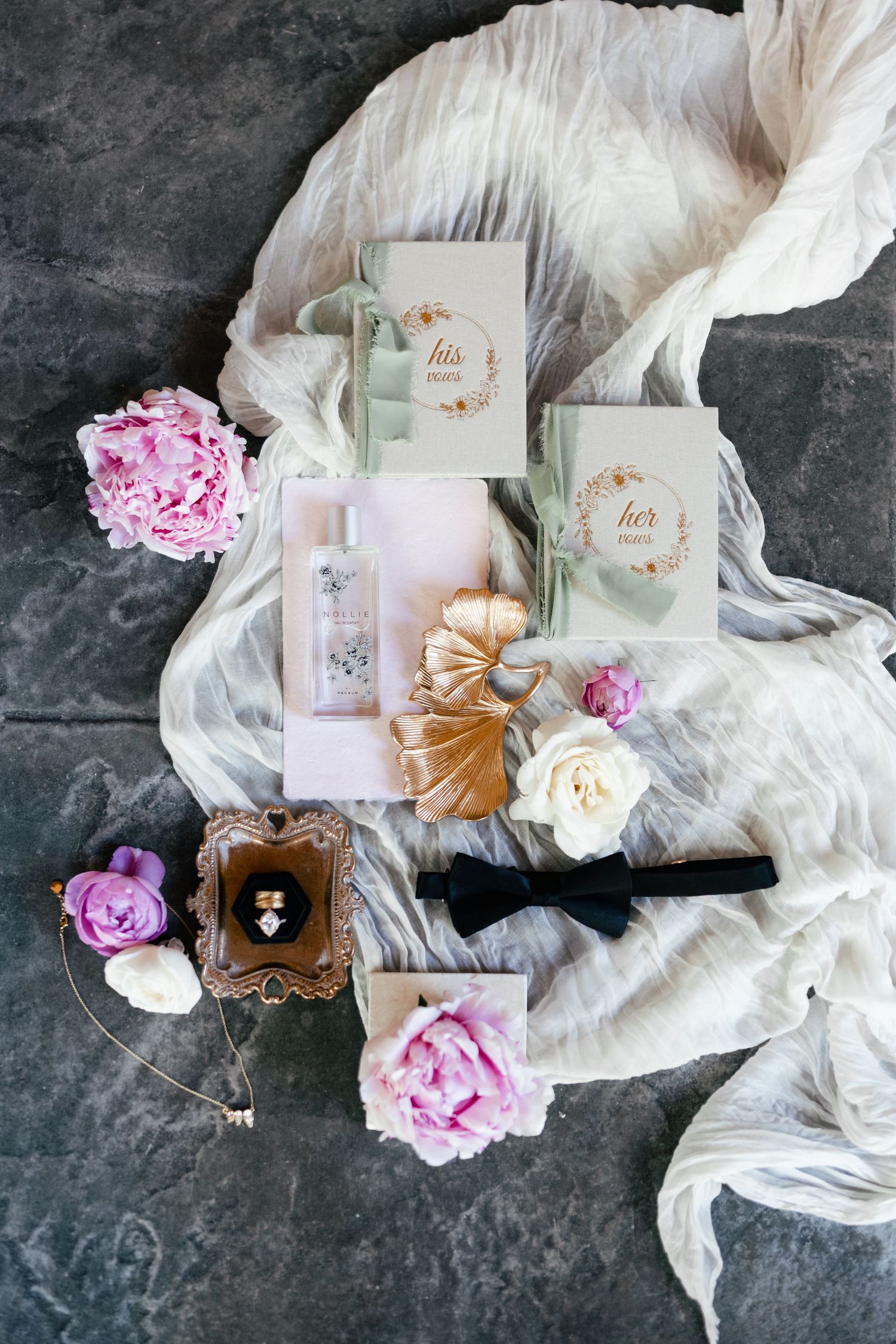Wedding invitations with romantic floral decorations, pink peonies, delicate ribbons and silk fabrics on dark stone background.