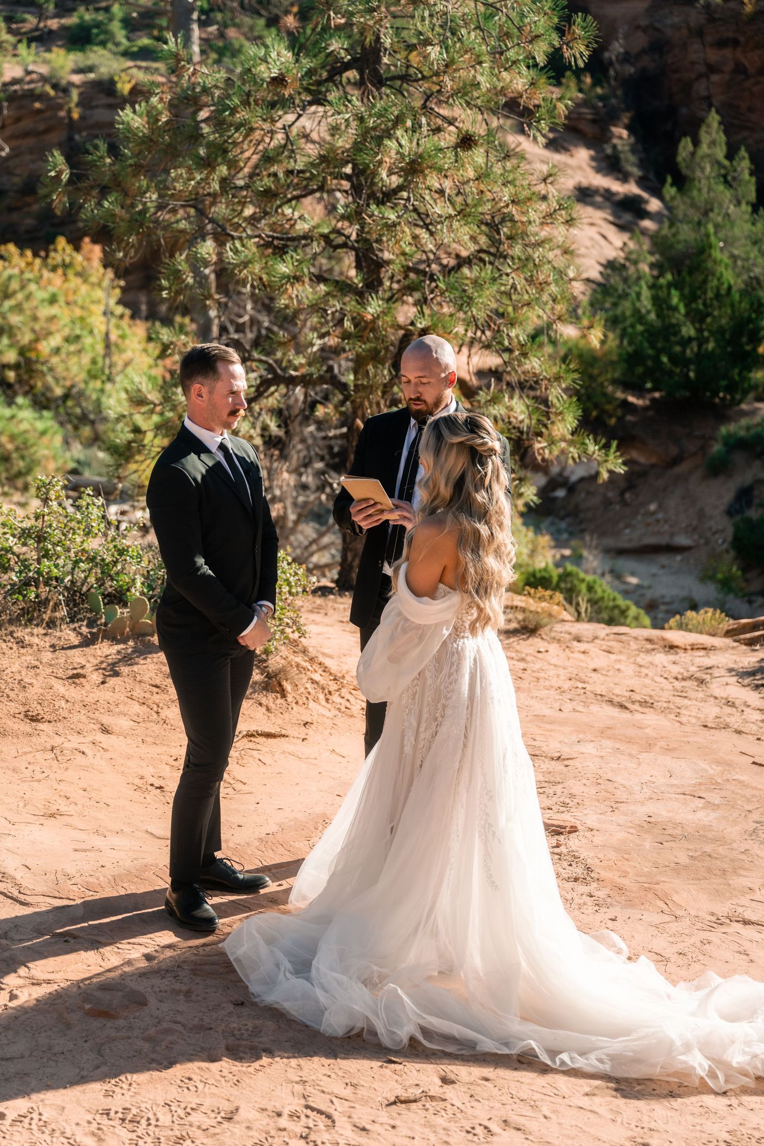 An intimate wedding ceremony takes place on a desert trail surrounded by pine trees.
