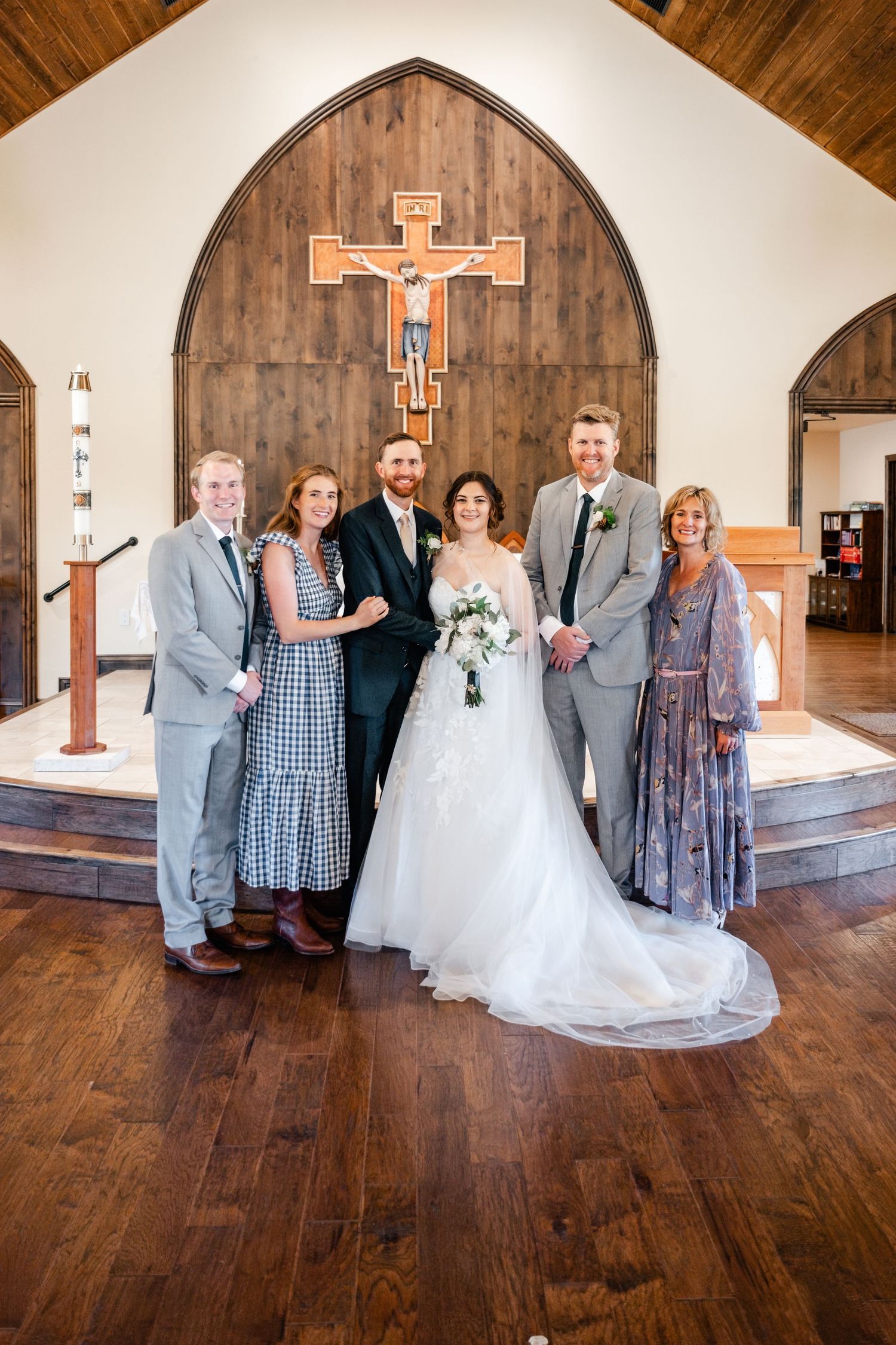 Wedding party poses in front of wooden church altar with large crucifix during traditional ceremony.