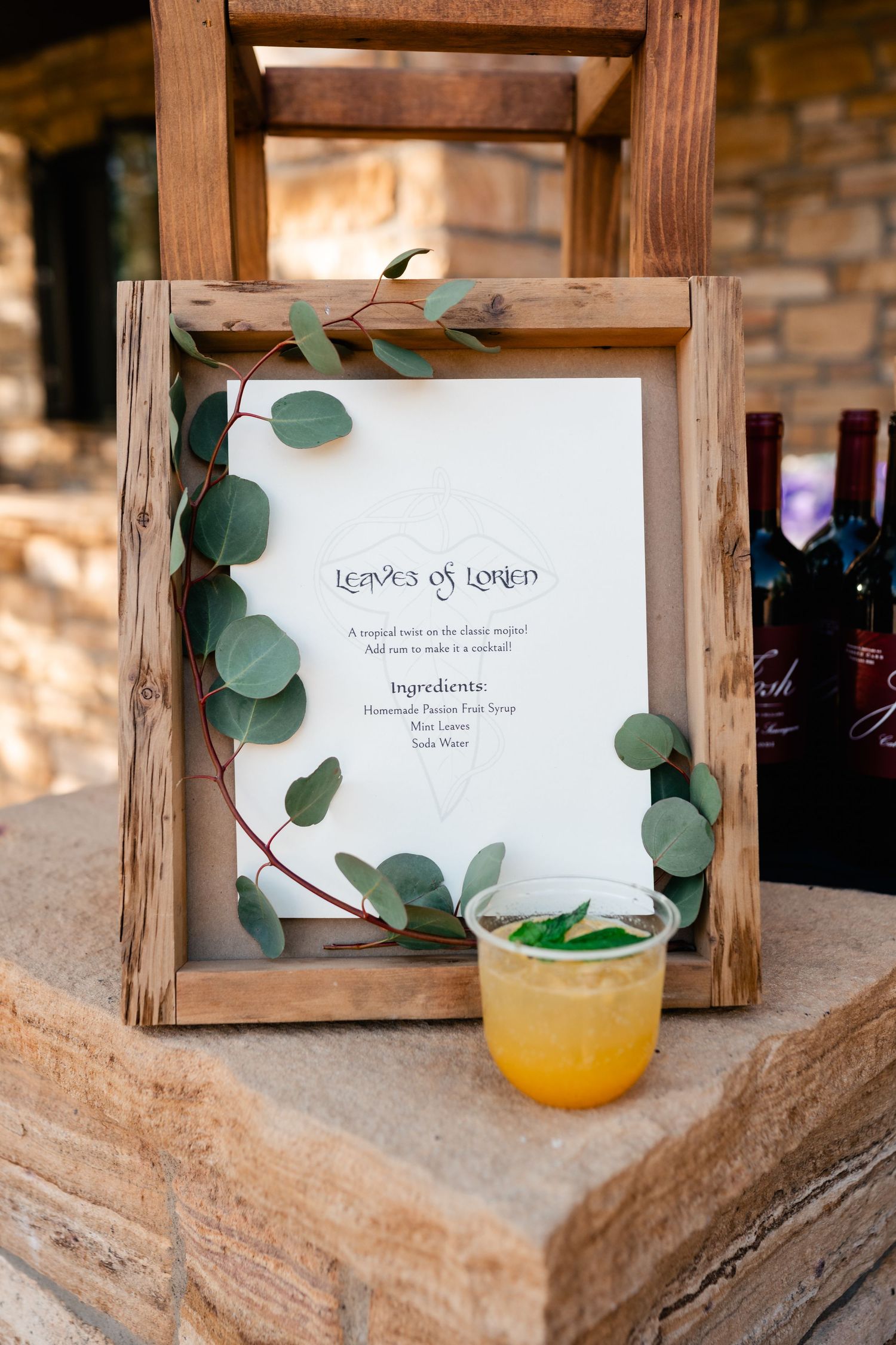 Rustic wooden frames with eucalyptus leaves display wedding signage and drink menus.