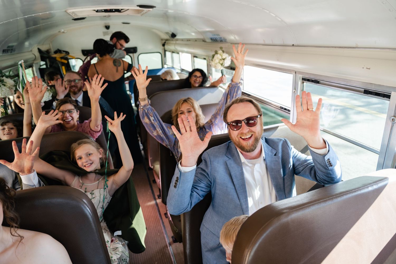 Excited passengers wave their hands in celebration while riding on a school bus.
