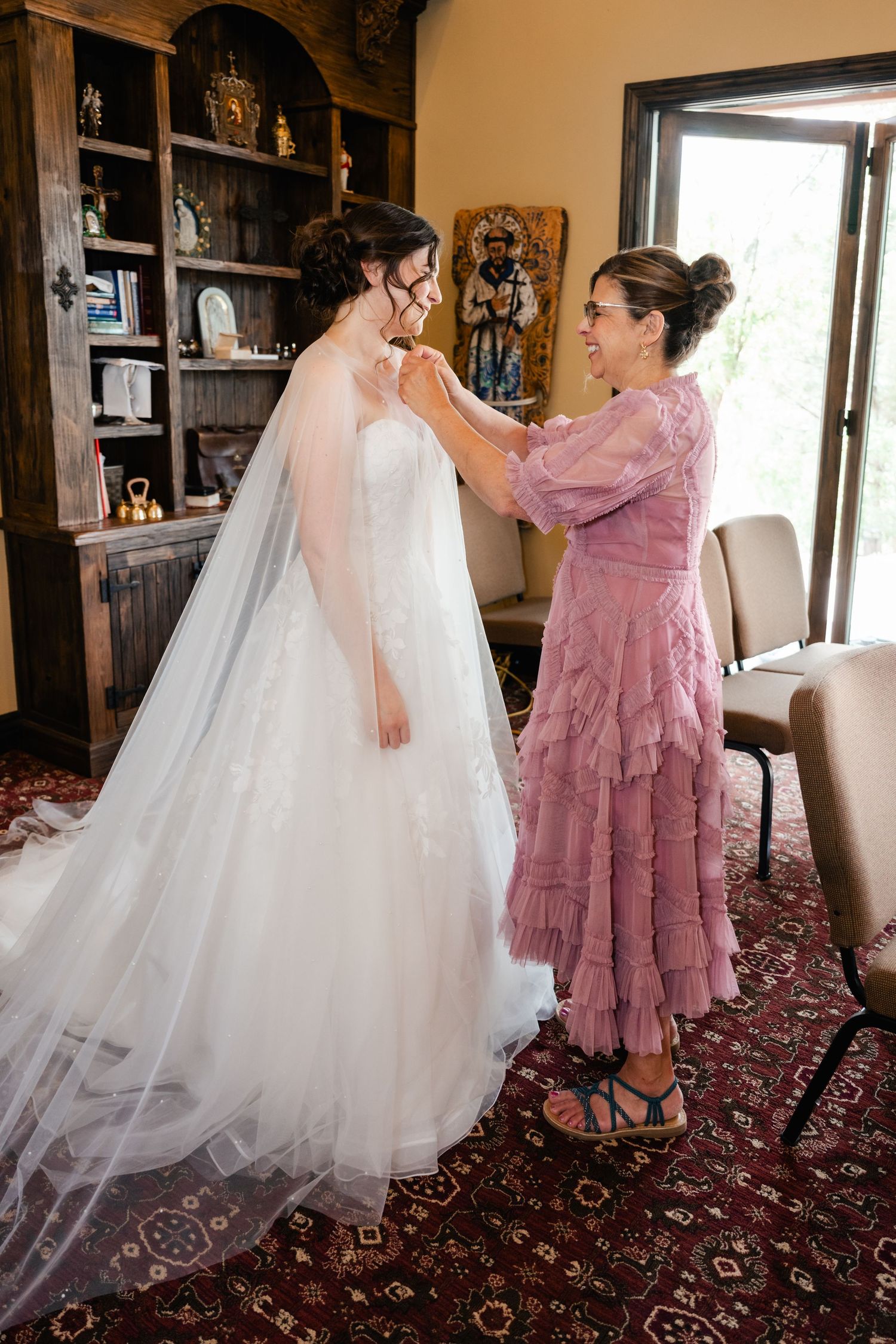 Helpers assisting with arranging a white wedding dress train on patterned carpet in indoor setting.