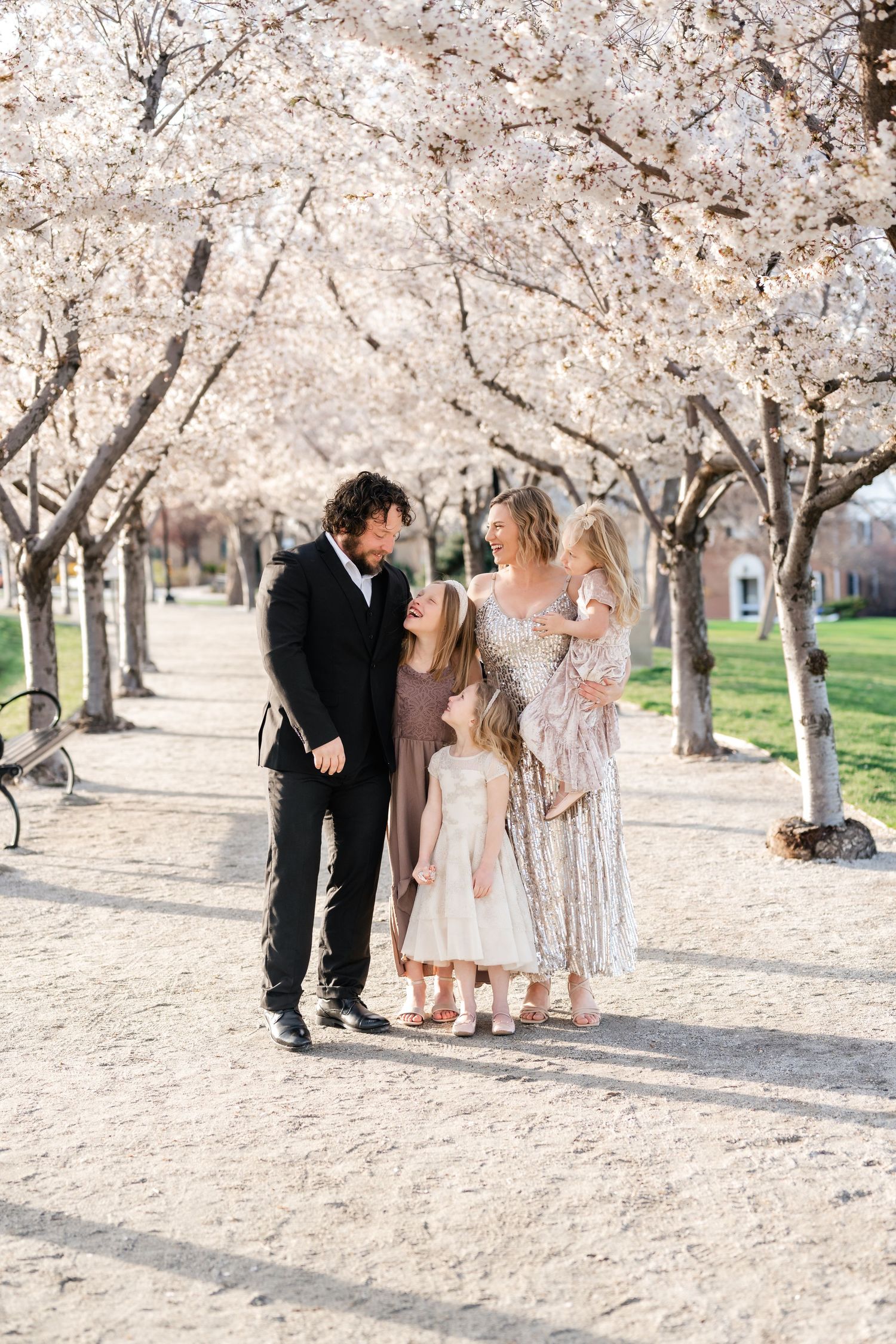 A family enjoys a spring day beneath blooming cherry blossom trees in a scenic outdoor setting. Utah Family Photographer.