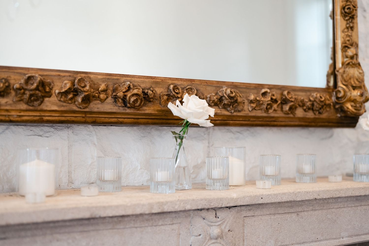 Row of white candles and floral decorations line a rustic wooden mantel.