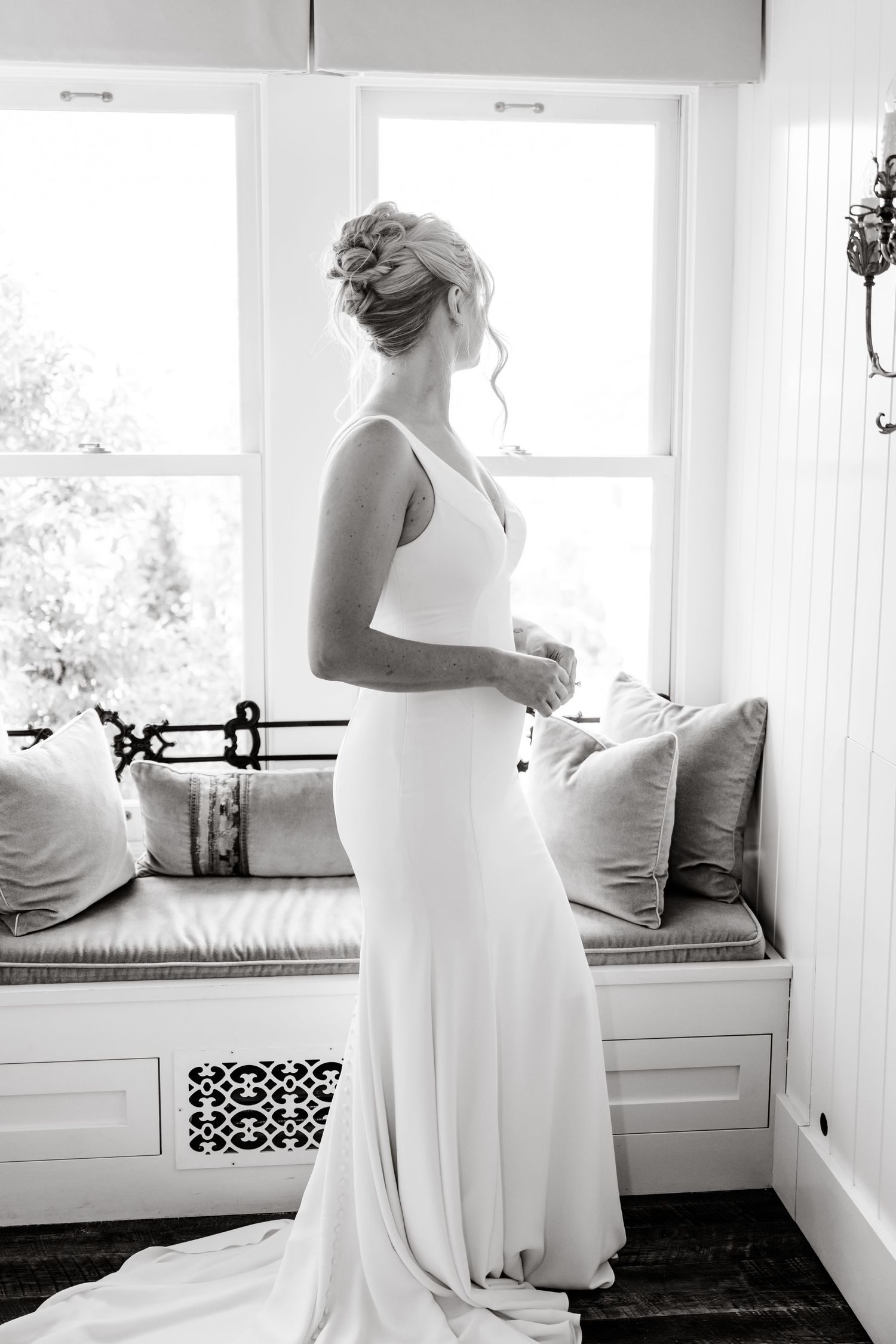 Elegant white wedding dress silhouette by a window with built-in bench seating.