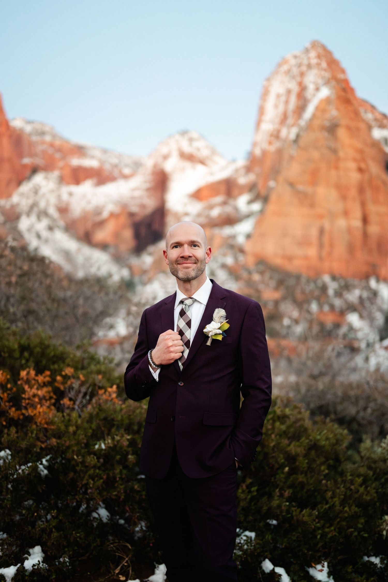 Person in purple suit poses against snow-capped red rock mountains on a clear day.