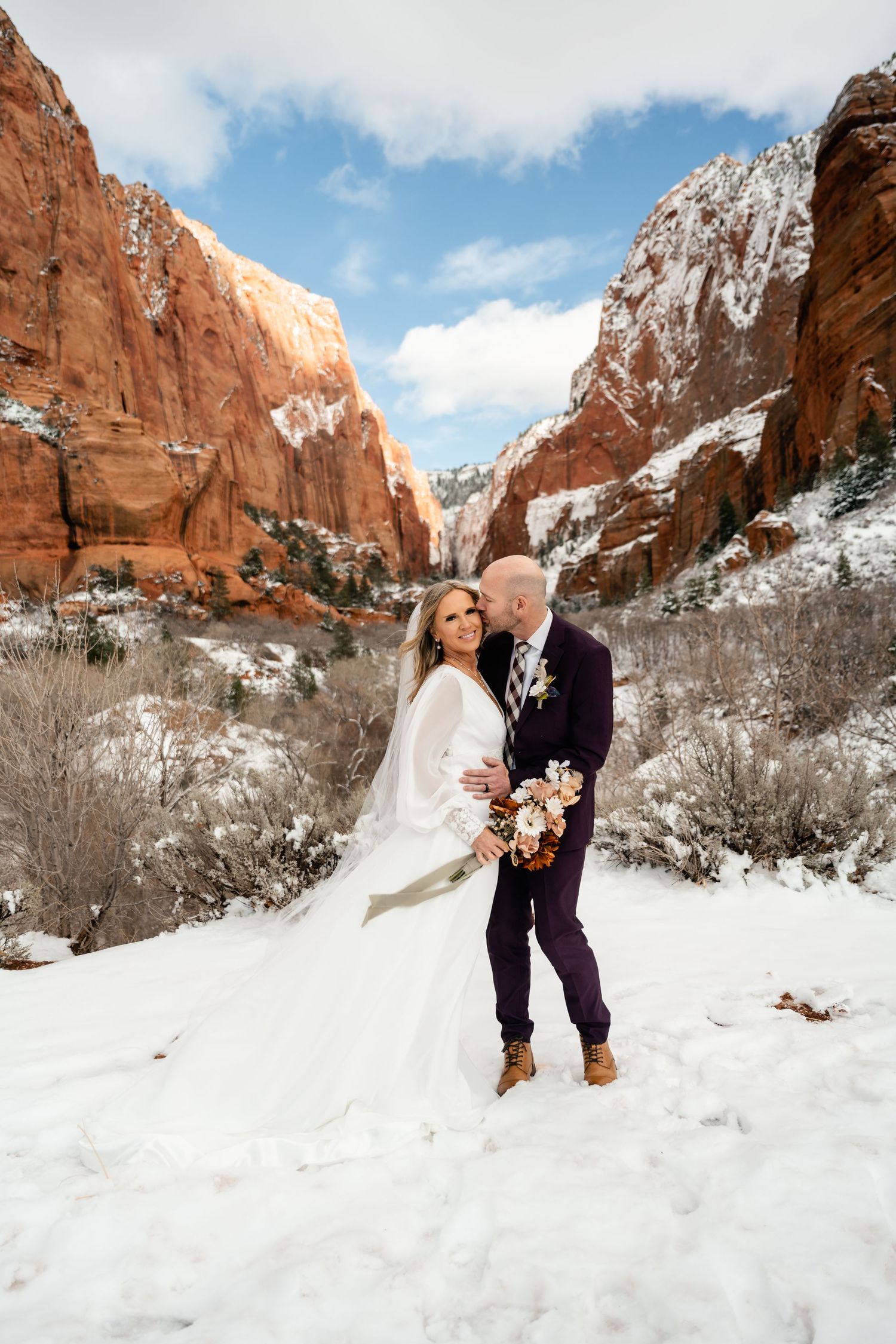 A winter wedding photoshoot in a snow-covered canyon with dramatic red rock cliffs and blue skies.