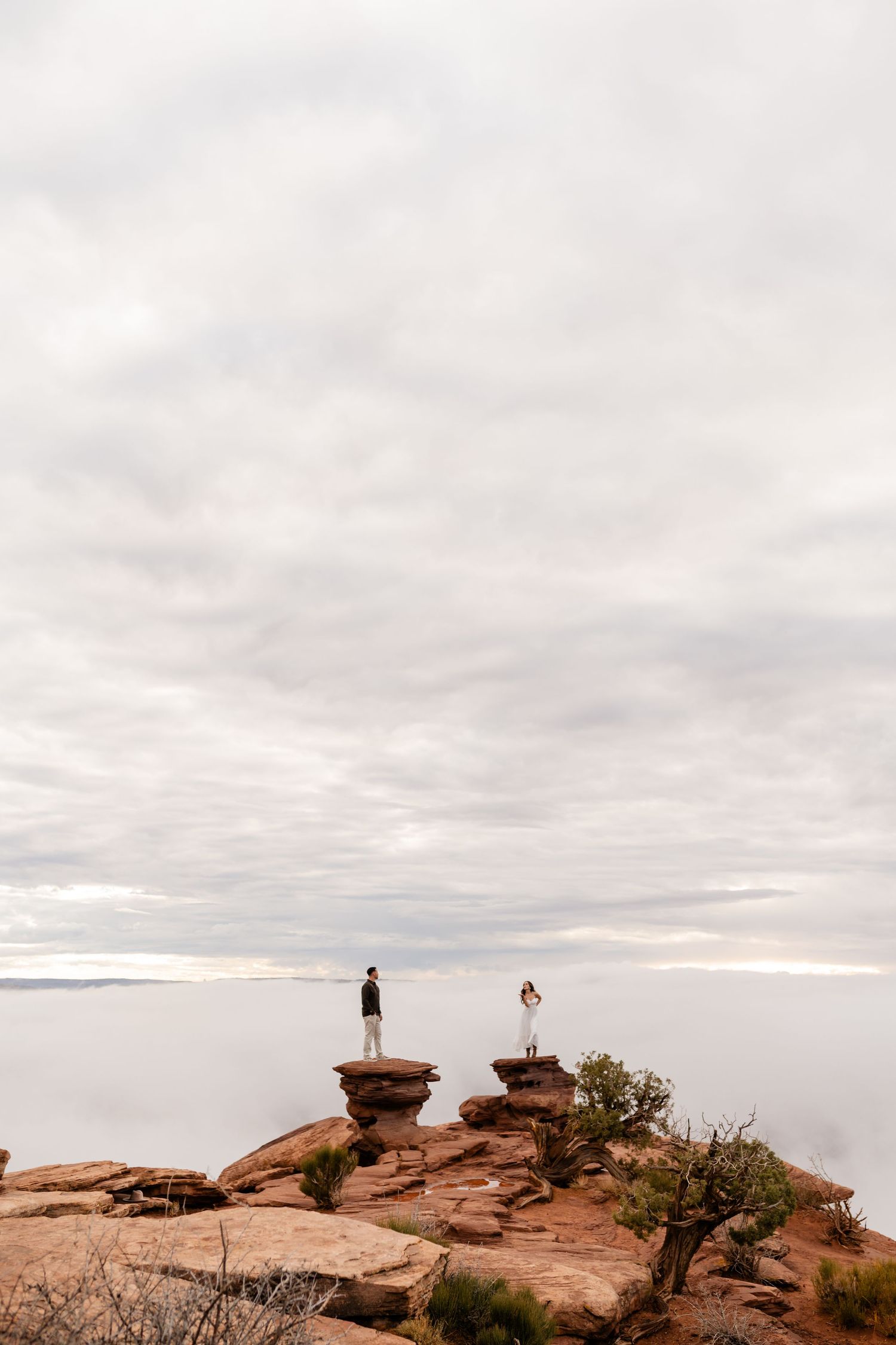 Two silhouettes stand on separate rock formations against a cloudy sky.