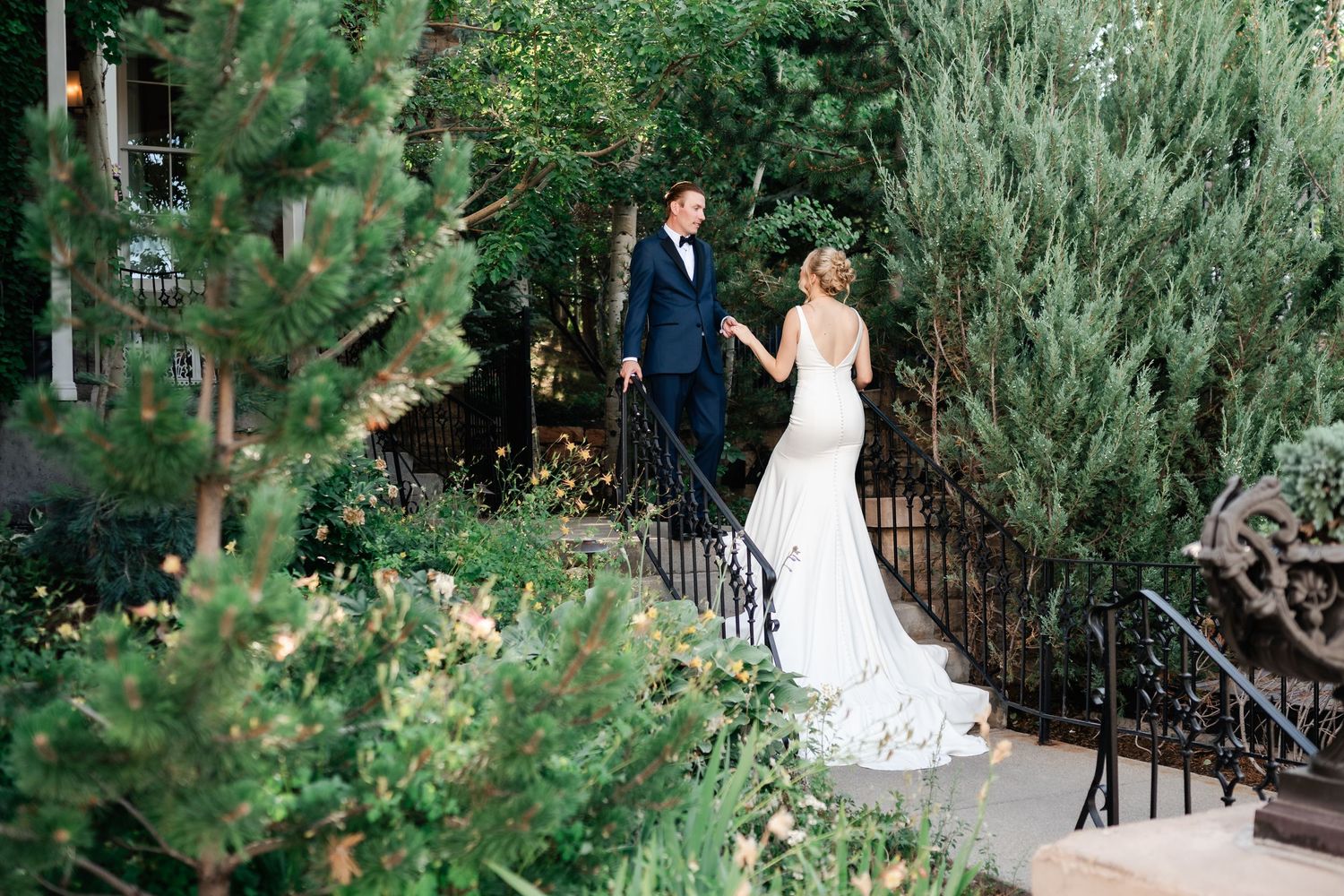 Bride and groom share a romantic moment on garden stairs surrounded by lush greenery at an elegant Park City wedding venue.